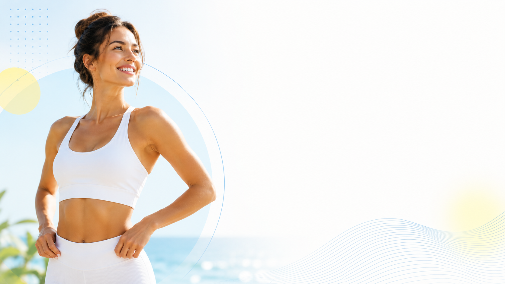 A smiling woman in a white sports top and leggings standing outdoors with a beach and ocean in the background.