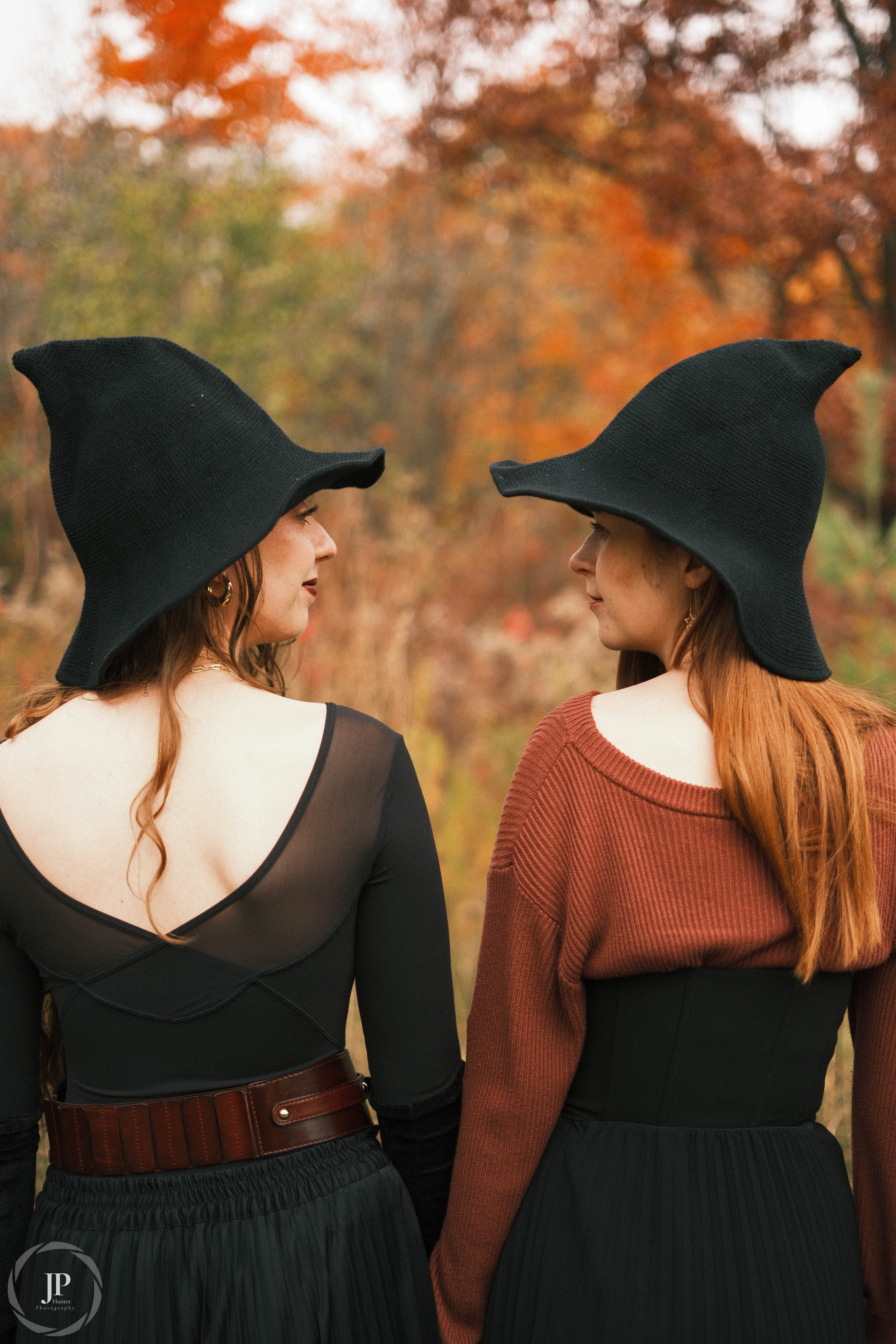 Two women in black pointed hats and autumn forest background