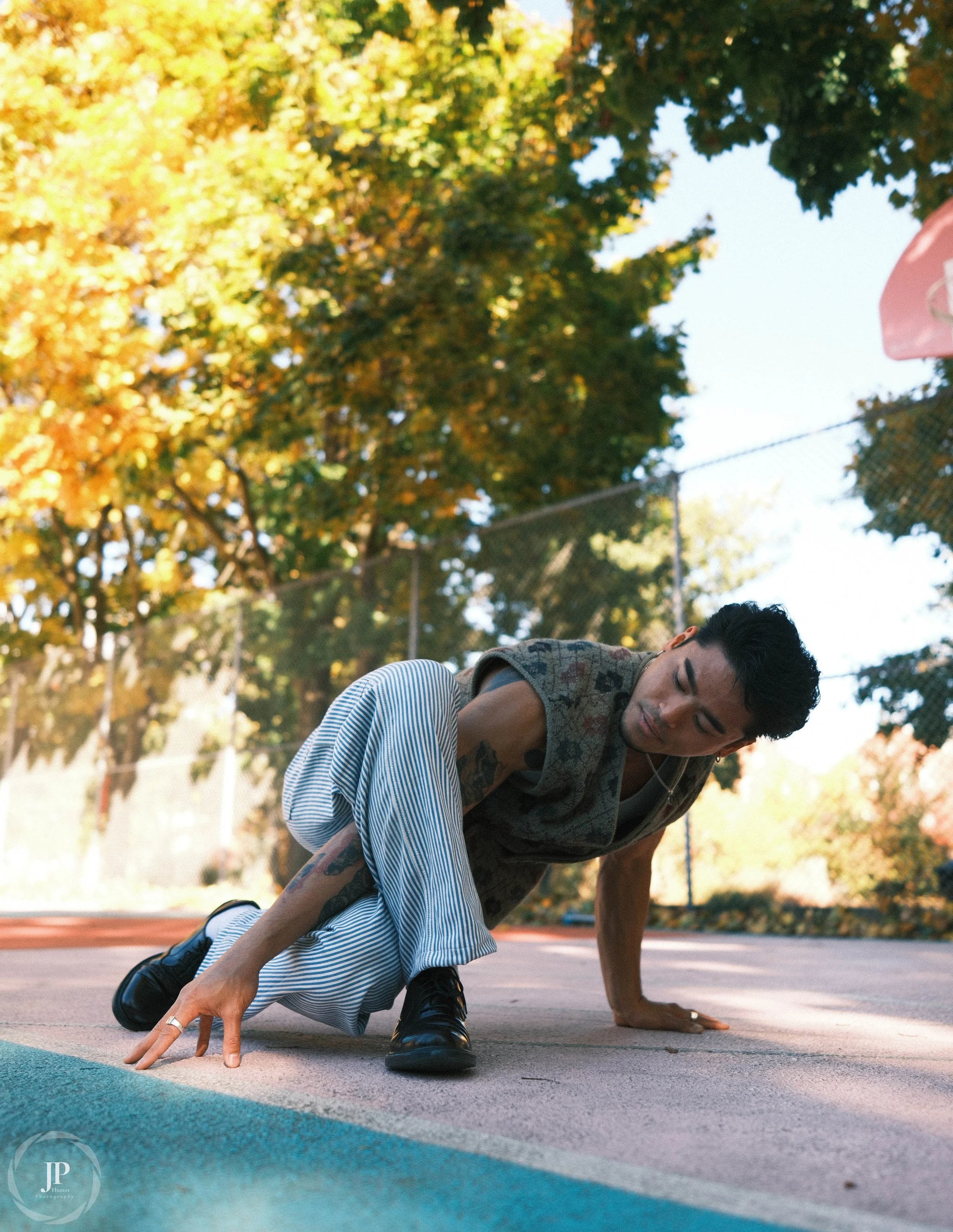 Person posing in a break position with trees in the background, wearing patterned sleeveless top and striped pants.