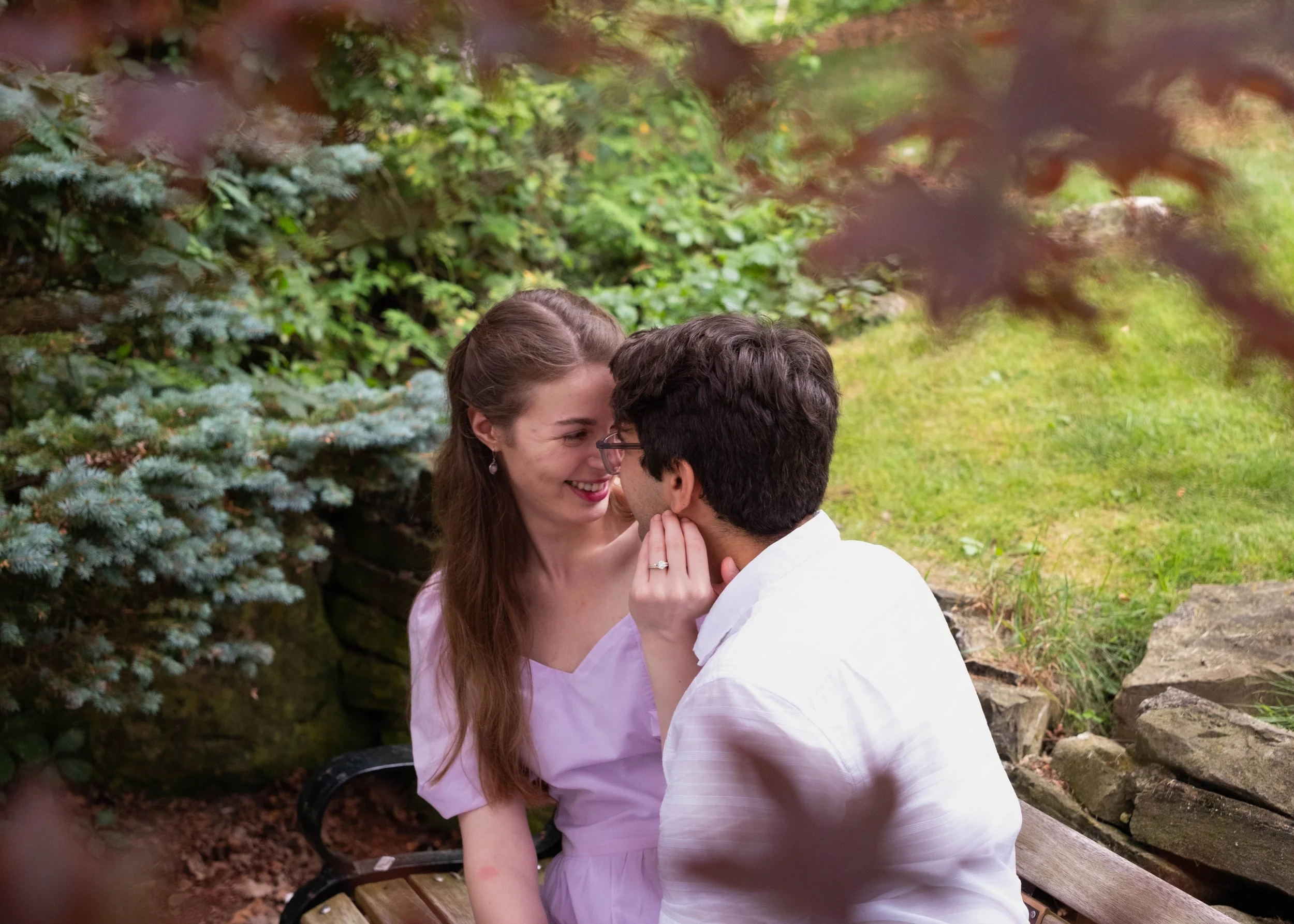 A couple looking lovingly into their eyes on a bench in a park with leaves in the foreground