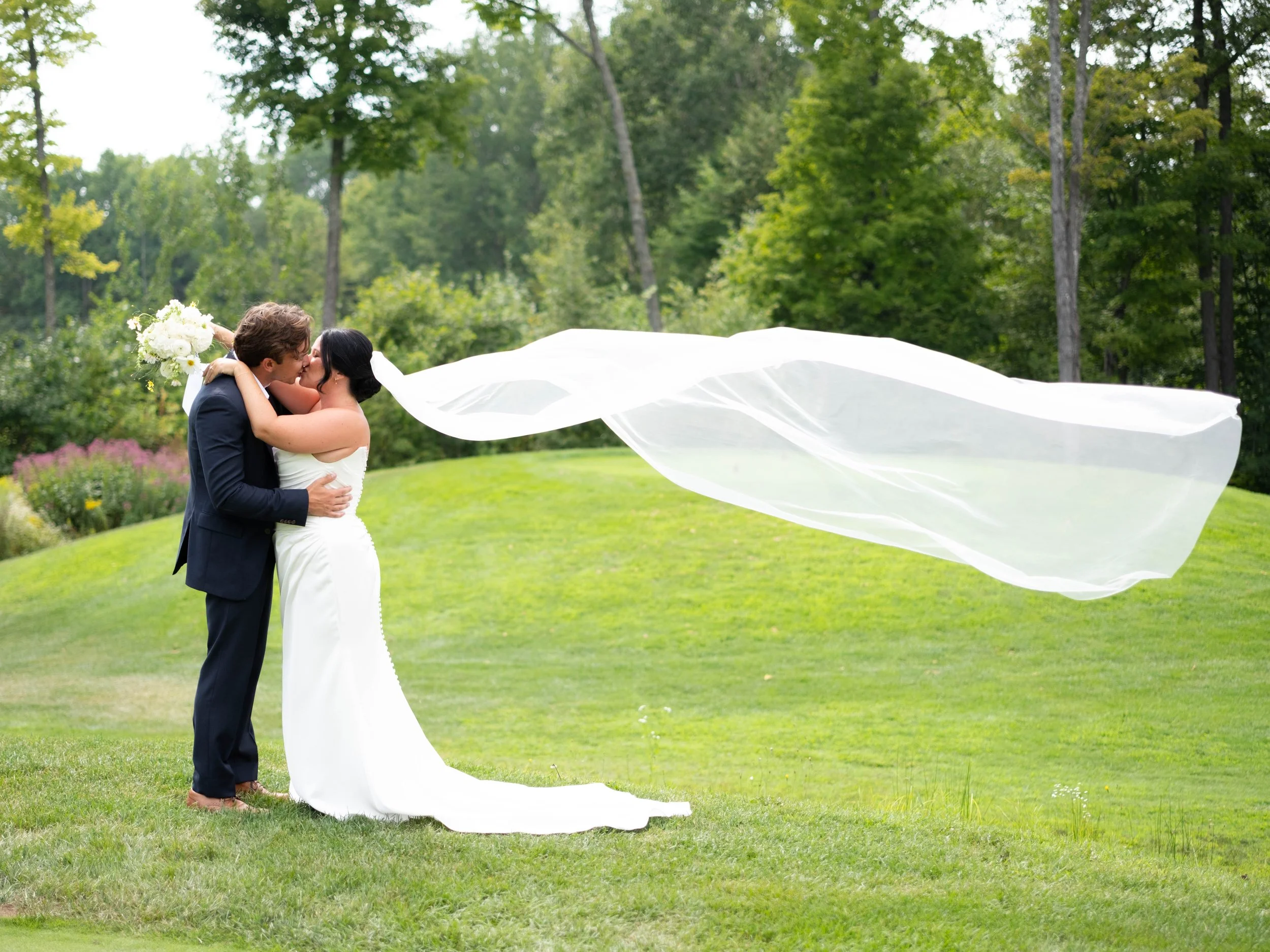 An artistic photo of the veil floating in the wind as the couple kisses on a golf course