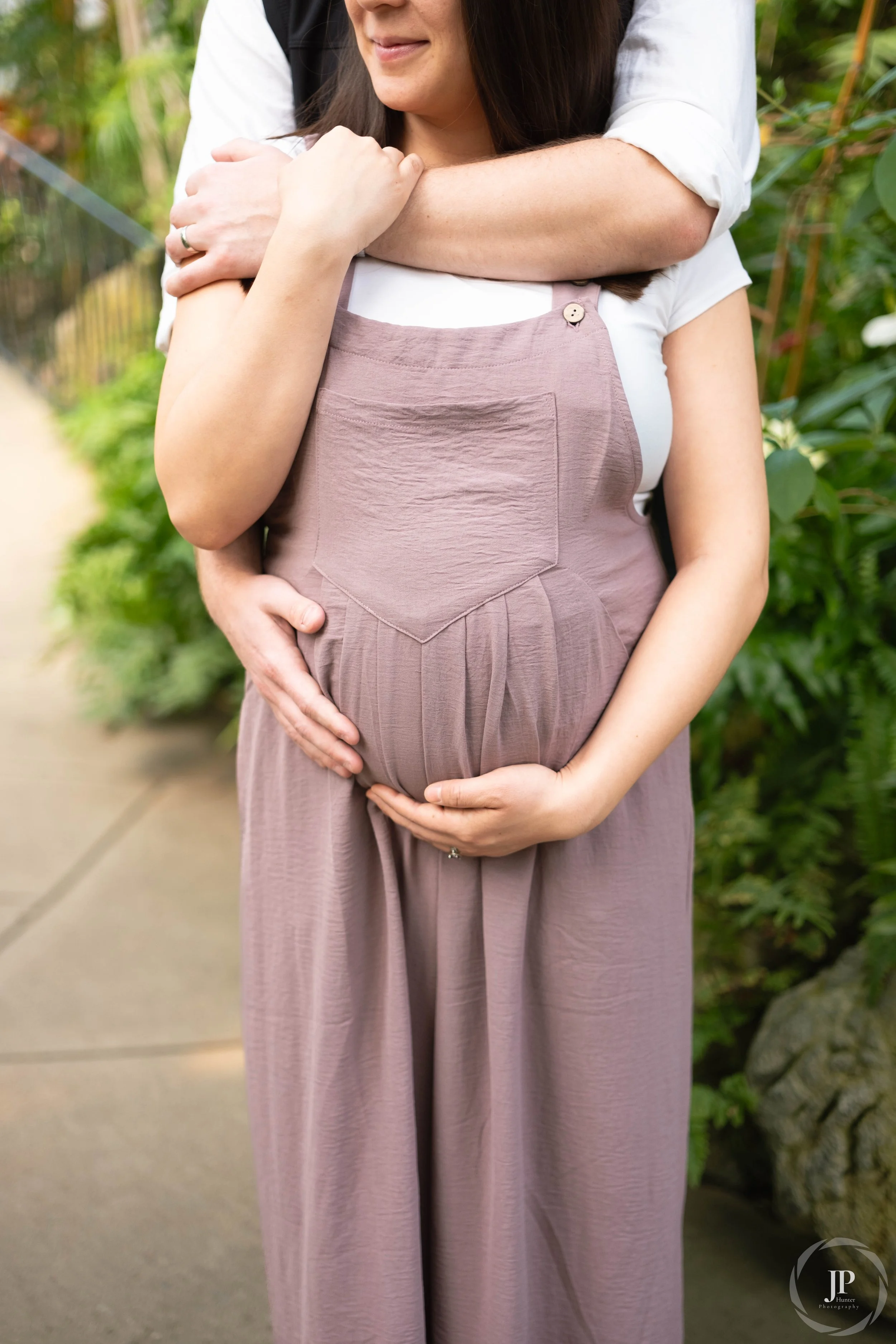 A couple posing for their maternity shoot in a greenhouse