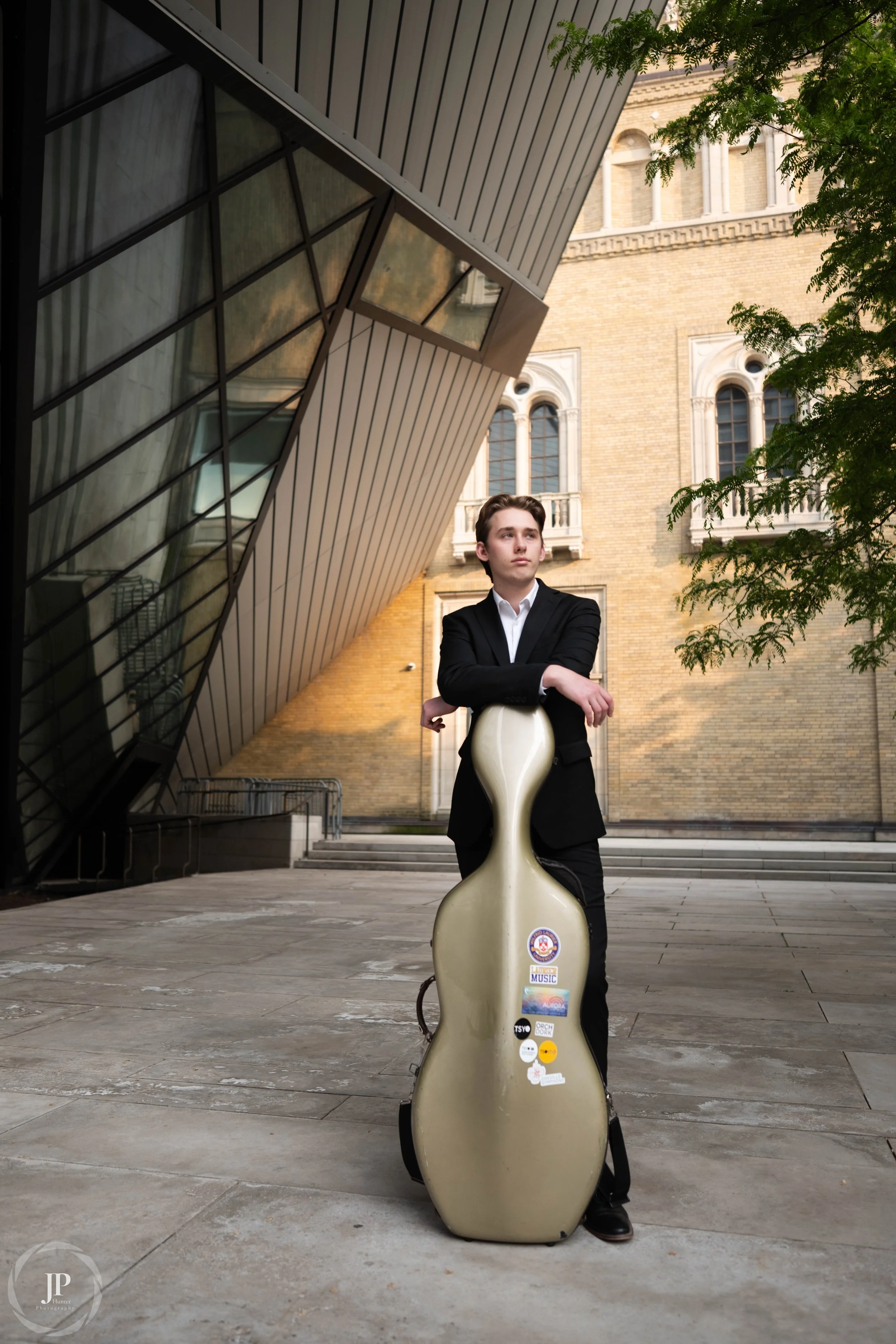 A person standing with his cello in front of the ROM in Toronto