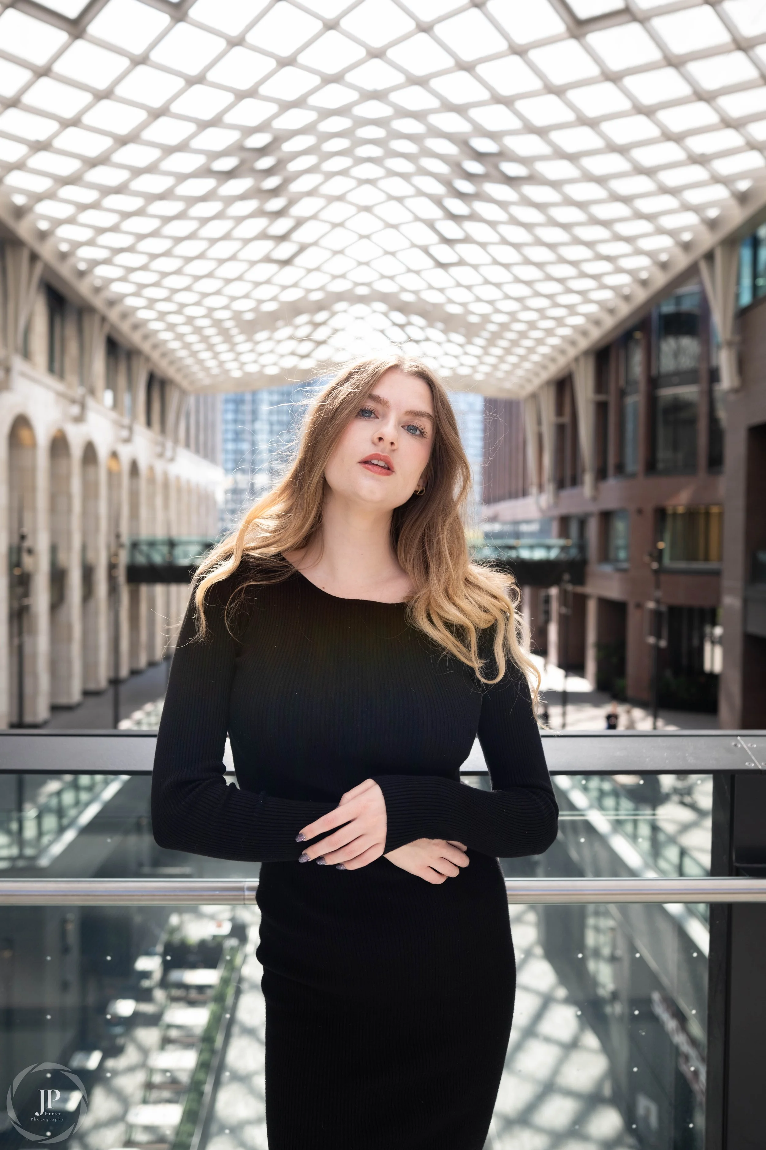Woman in black dress standing in a modern architectural setting with a geometric ceiling and glass railings.