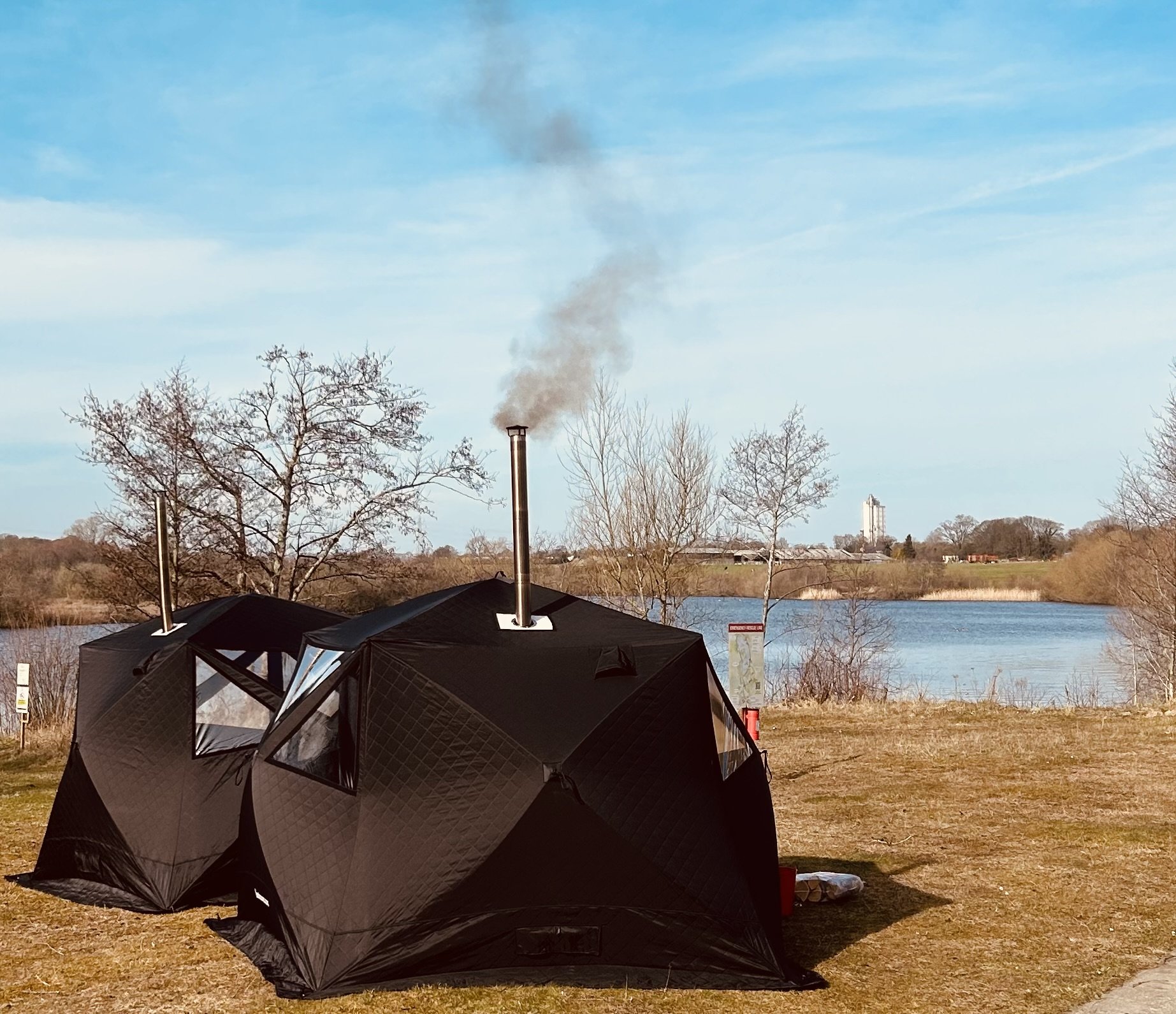 Black saunas with chimneys by a lake under a blue sky.