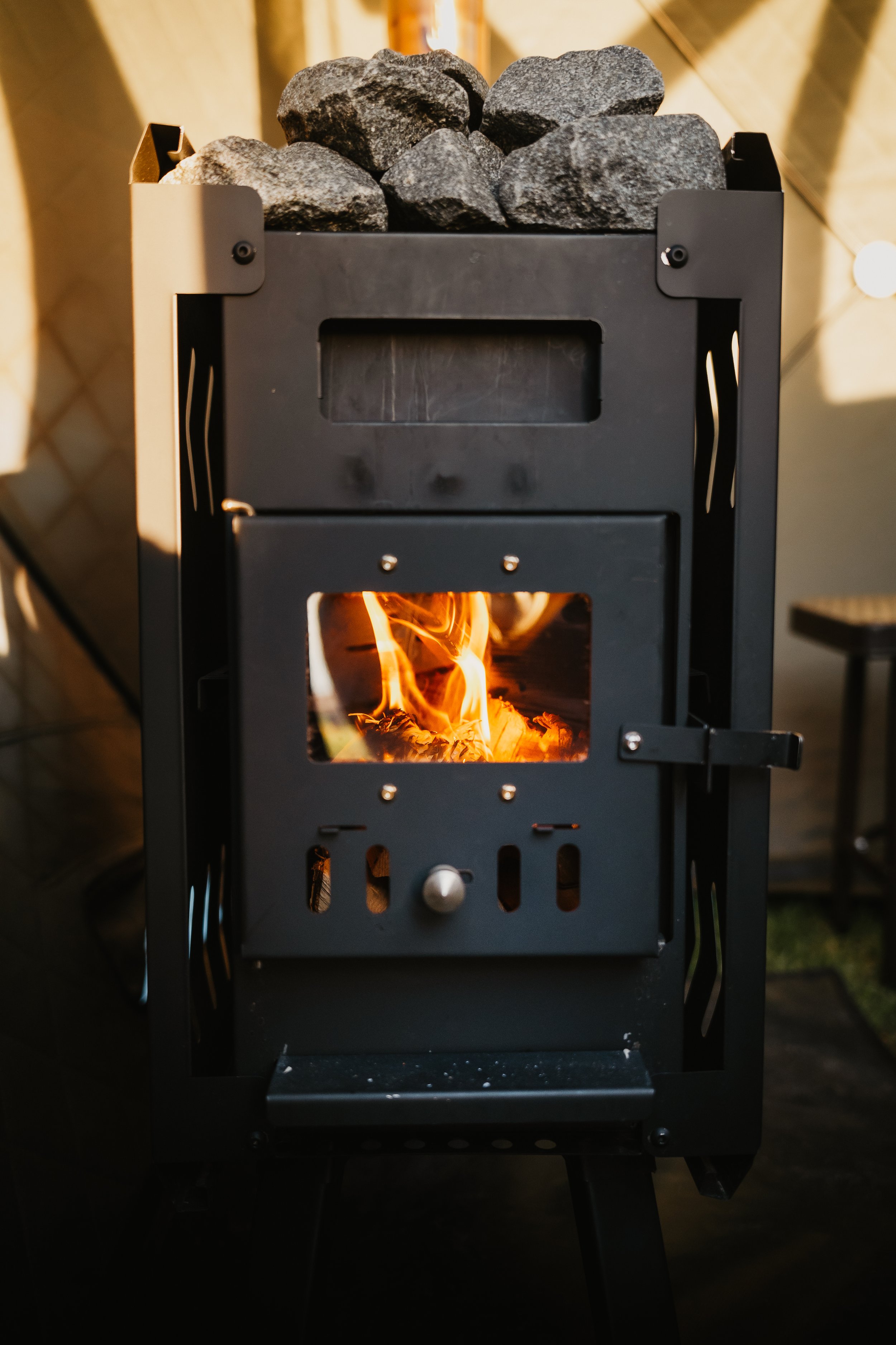 A wood-burning sauna stove with fire and stones on top
