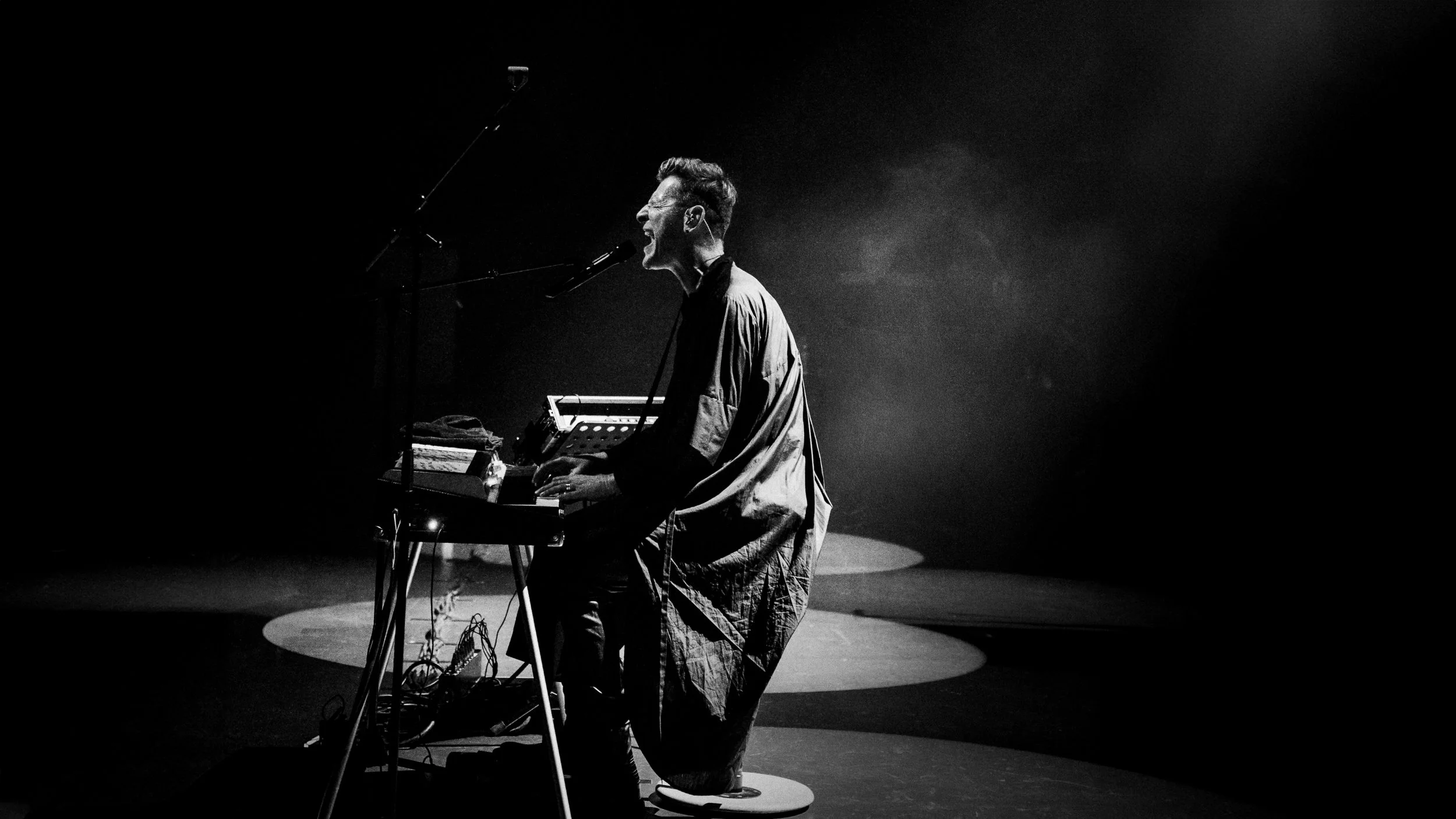 Black-and-white photo of Ozark Henry singing and playing keyboards on a dimly lit stage.