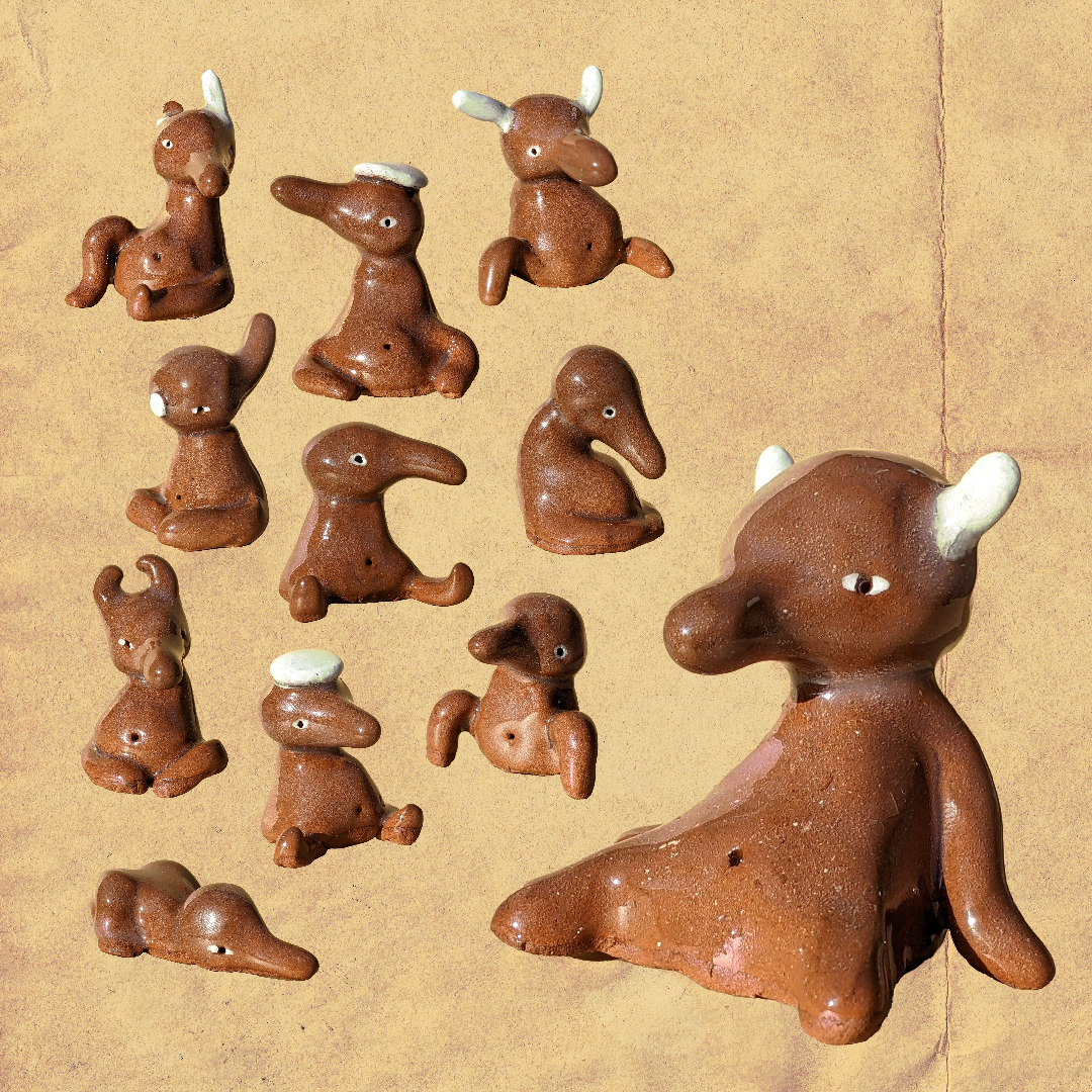 Collection of small, brown animal figurines resembling mice, rabbits, and a larger animal, all with simplistic features and white accents on their ears or heads, arranged on a tan background.