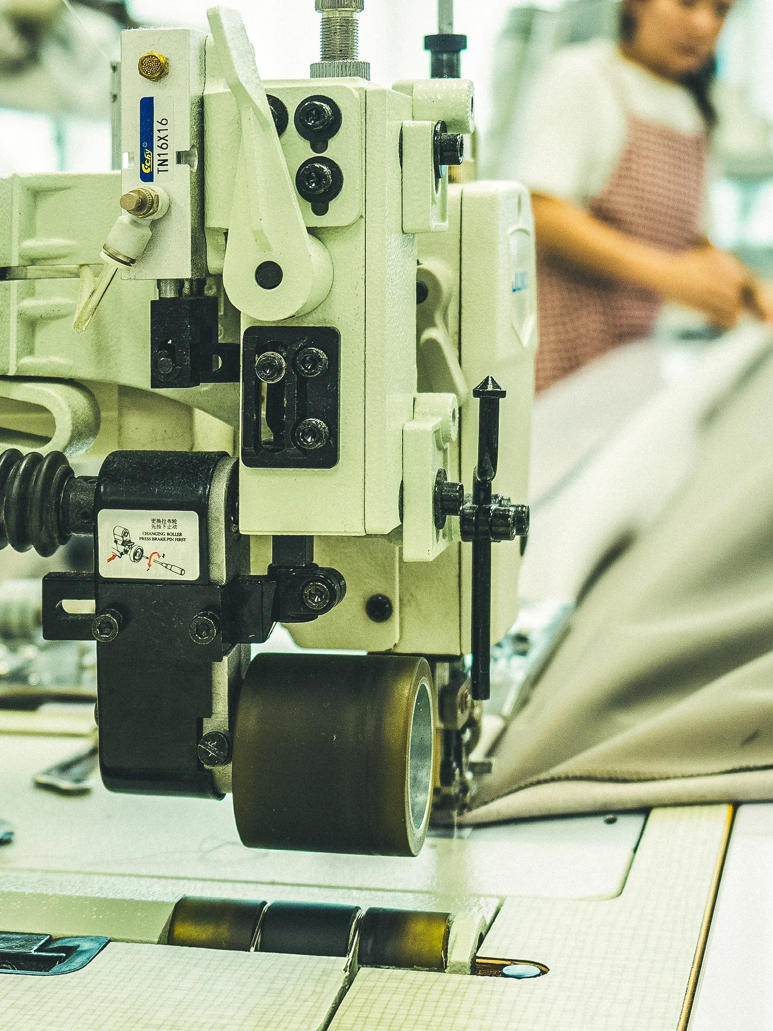 Industrial sewing machine in use with person in background working on fabric.