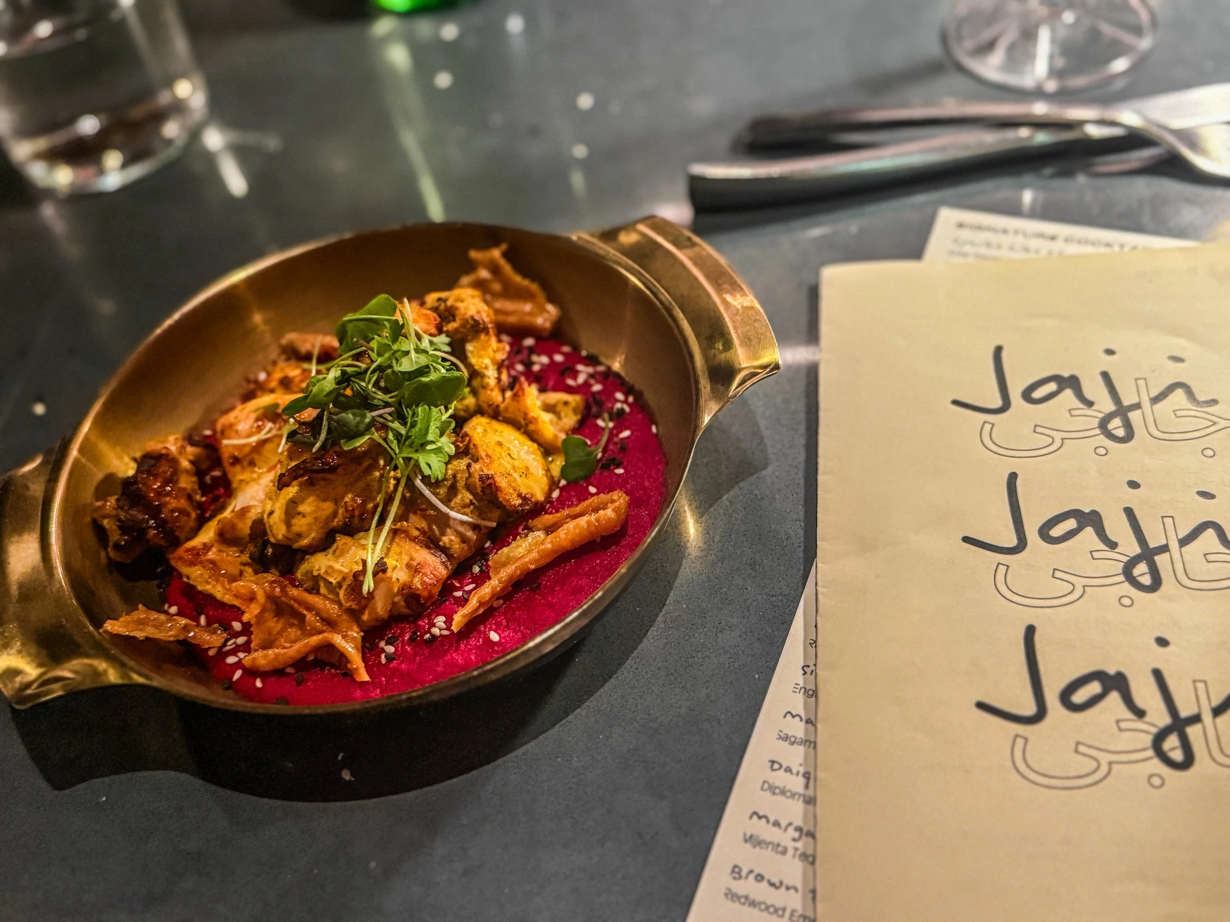 Four people toasting with colorful cocktails, including drinks garnished with dried citrus, mint leaves, and edible flowers.