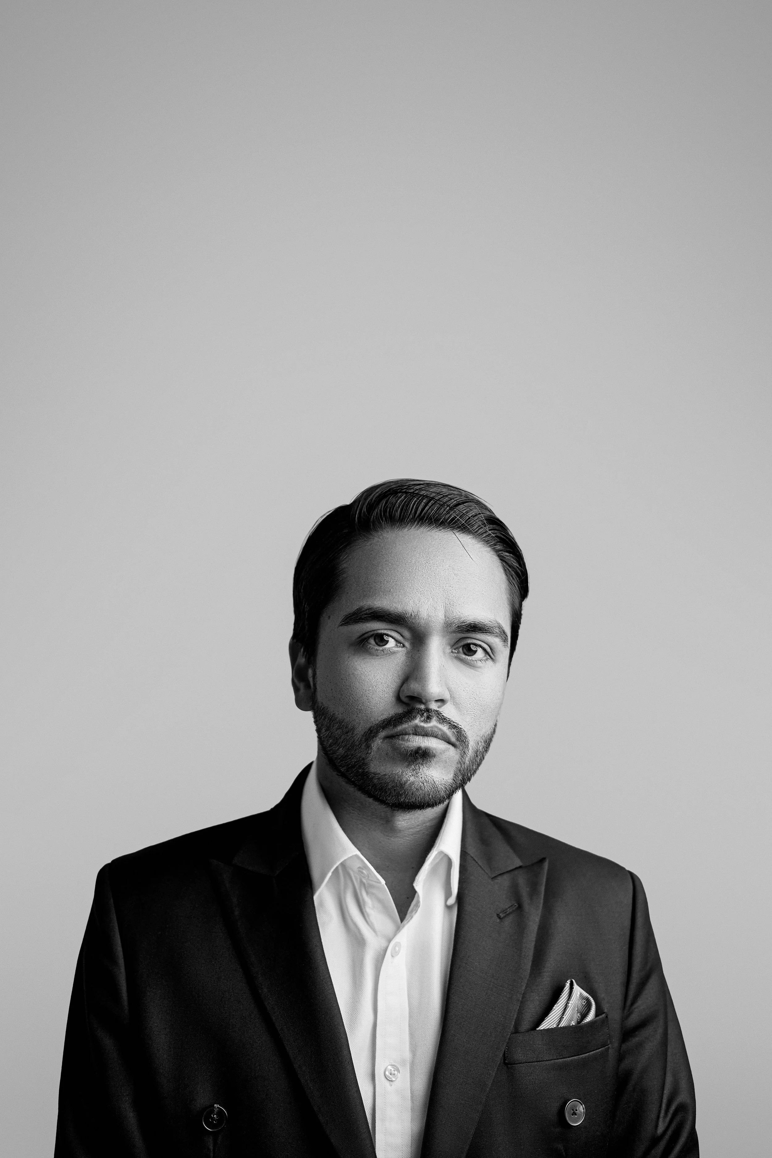 Black and white portrait of a man wearing a suit and tie, with slicked-back hair, looking directly at the camera.