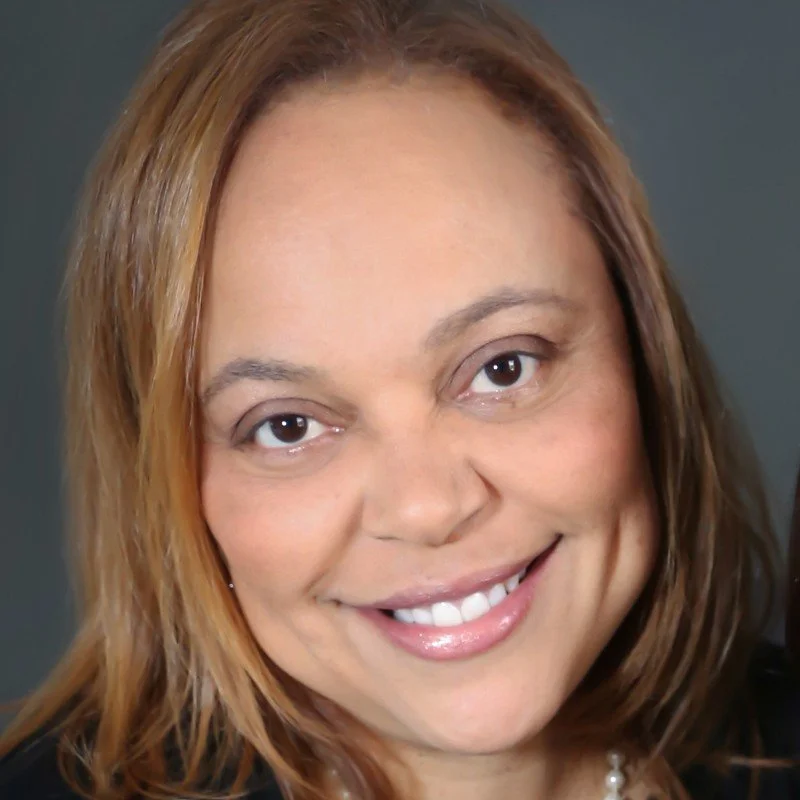 Close-up of a smiling woman with light skin and light brown hair against a plain background.