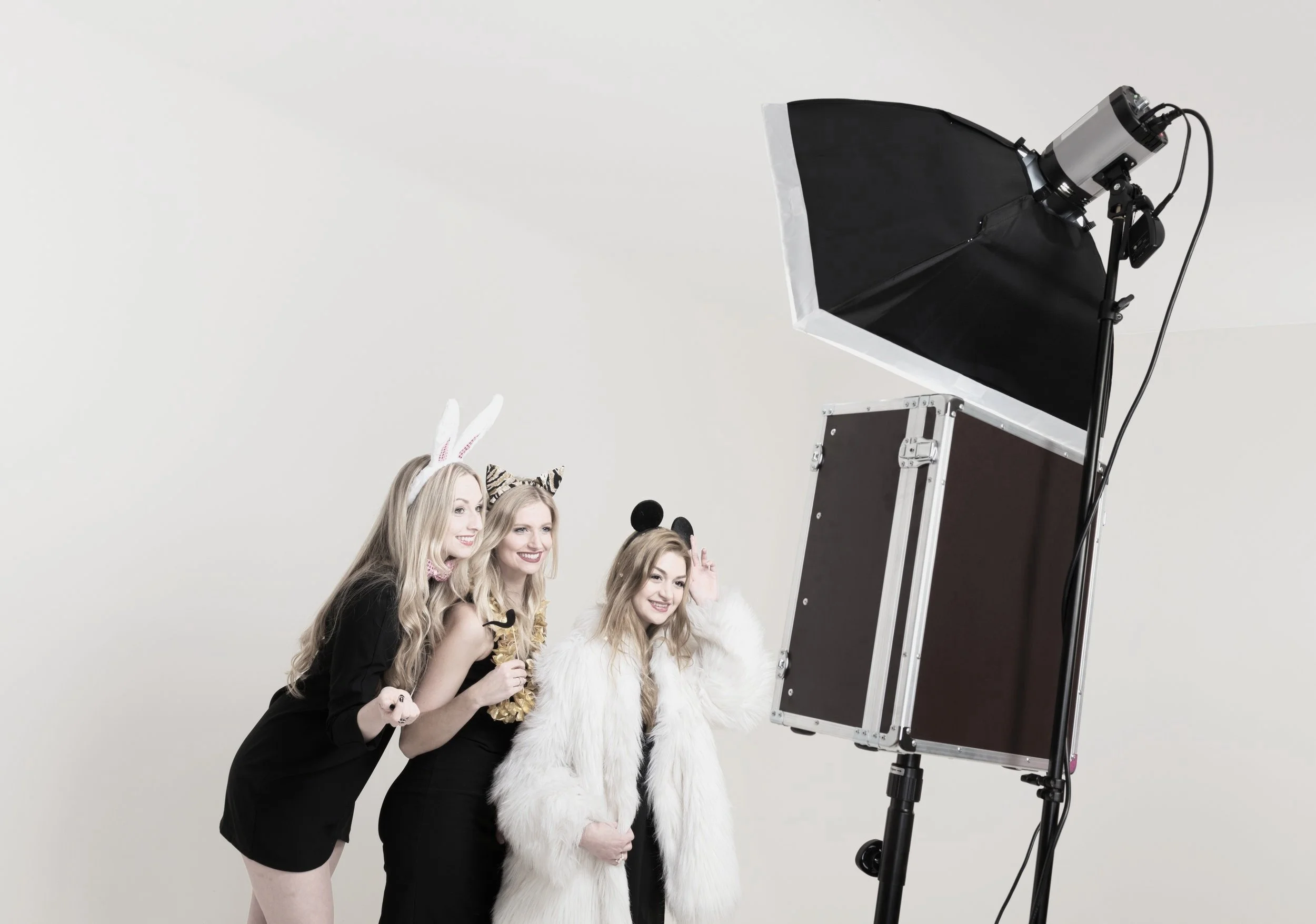 Three women in costumes taking a group photo with a photo booth on a plain white background.