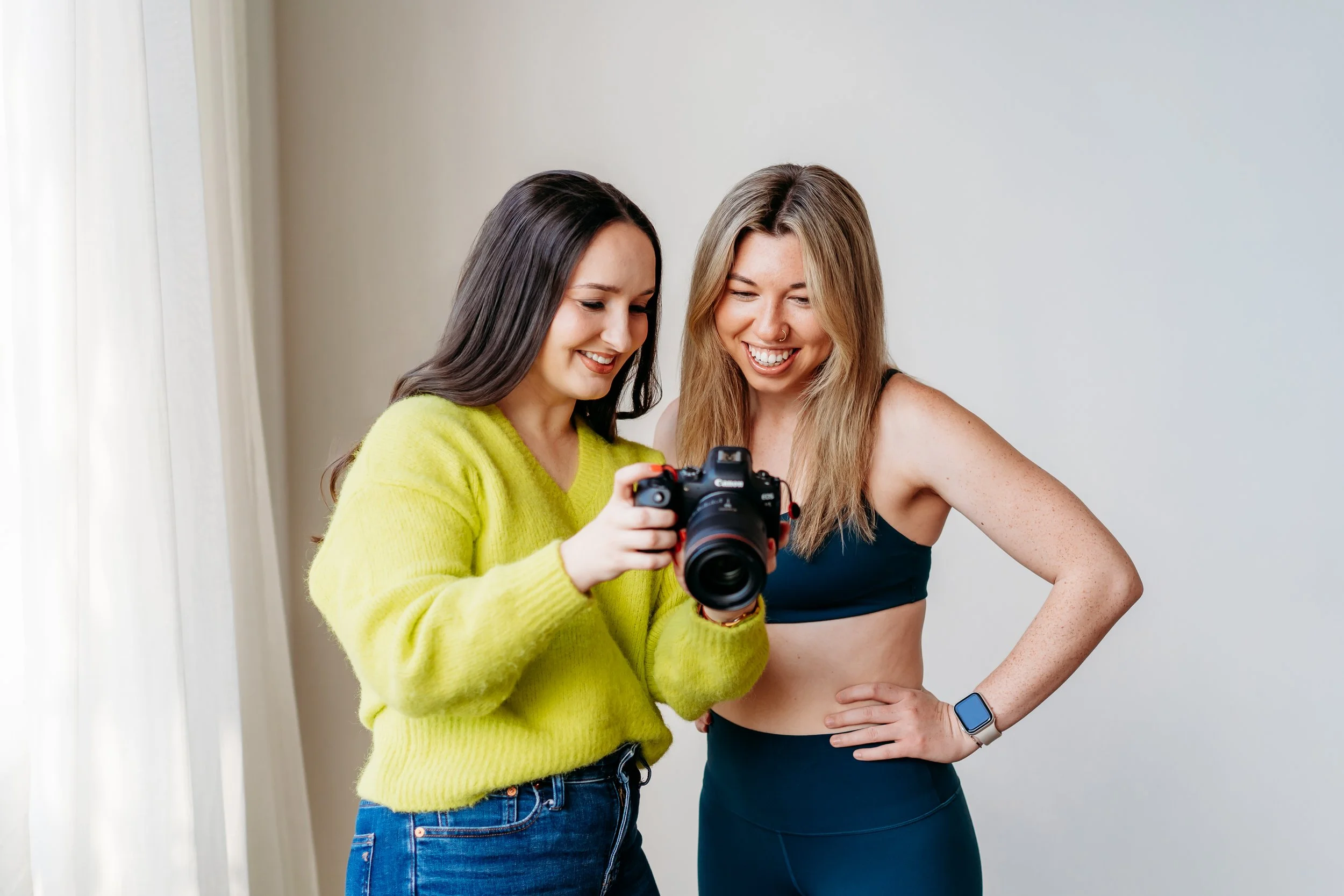 Two women smiling and looking at a camera screen.