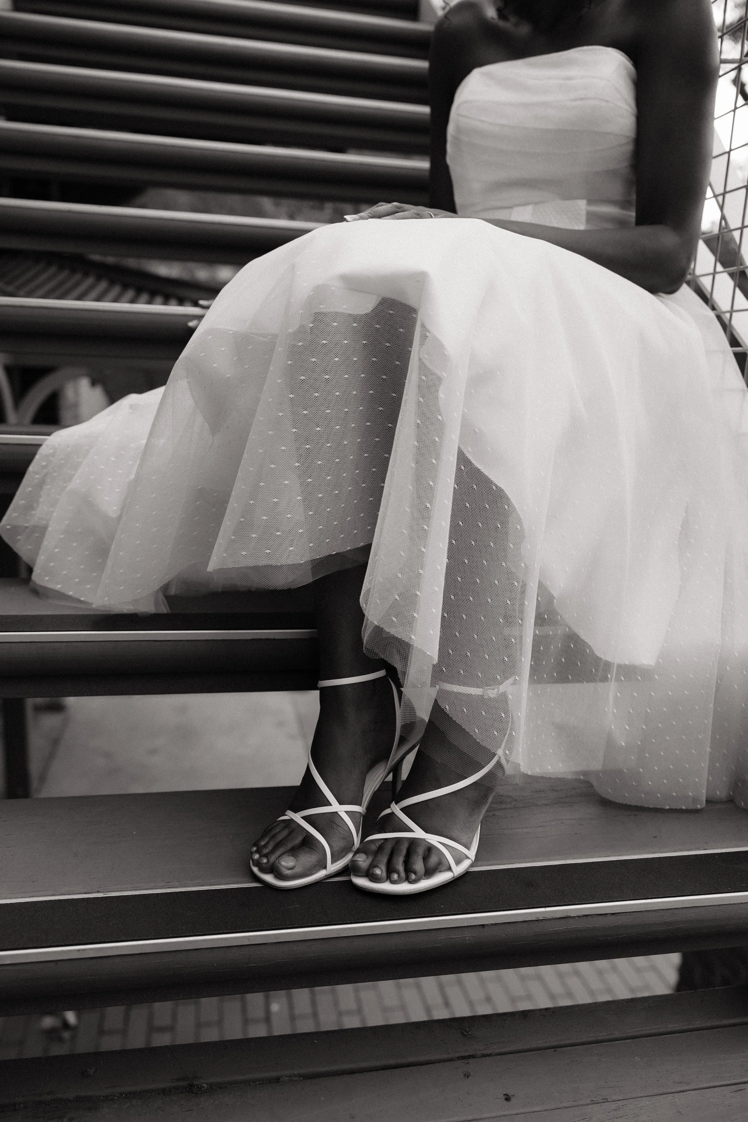 A bride sits on a staircase, the image is a close up of her strapped white sandals. Captured by Woodley Photography, an Adelaide Wedding Photographer. 