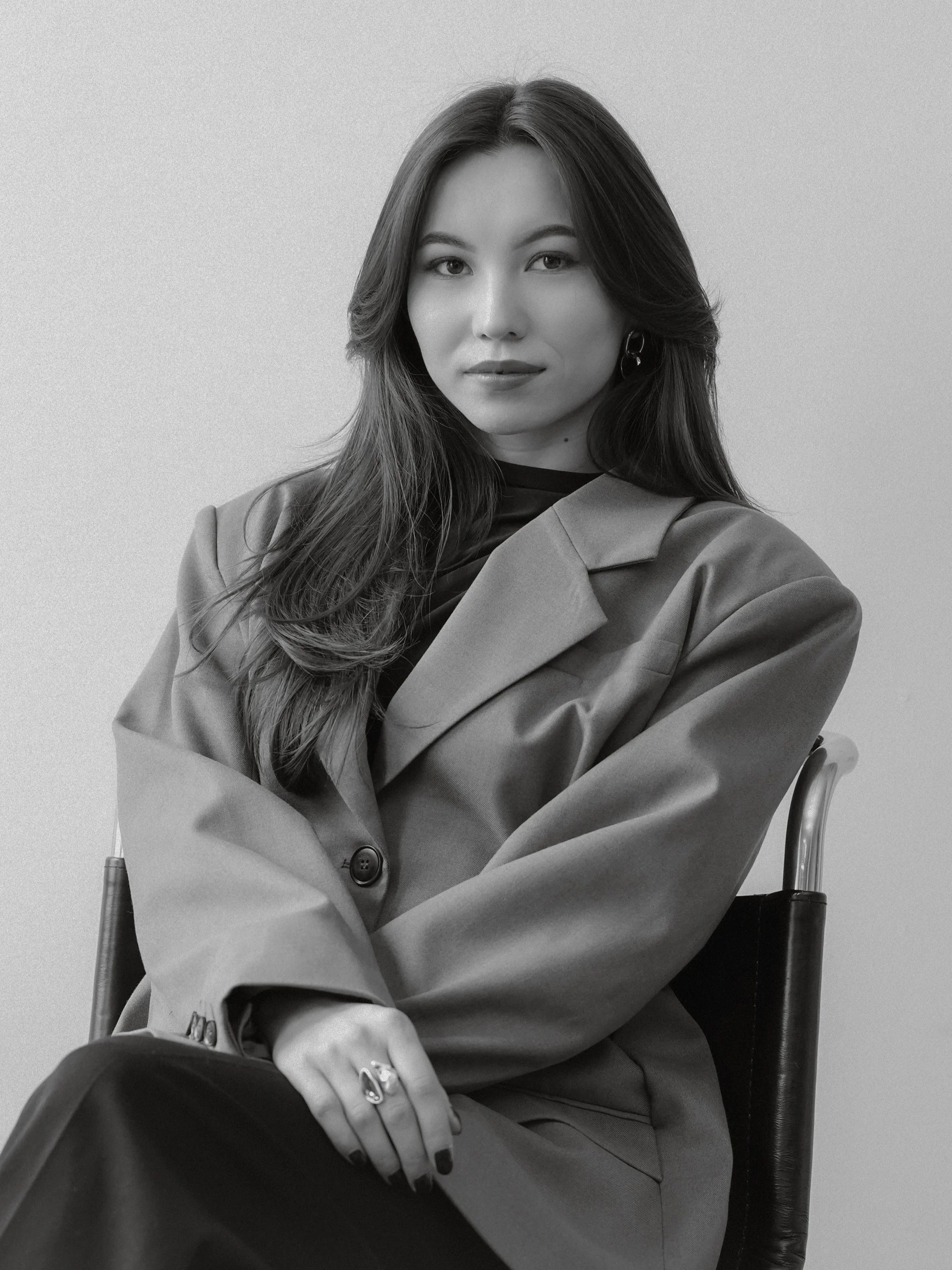 Black and white portrait of Mikaila Minna, founder of Minna Design House, seated in a chair wearing an oversized blazer.