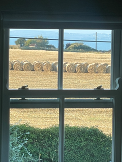 View through a window showing a field with large hay bales and a body of water in the background