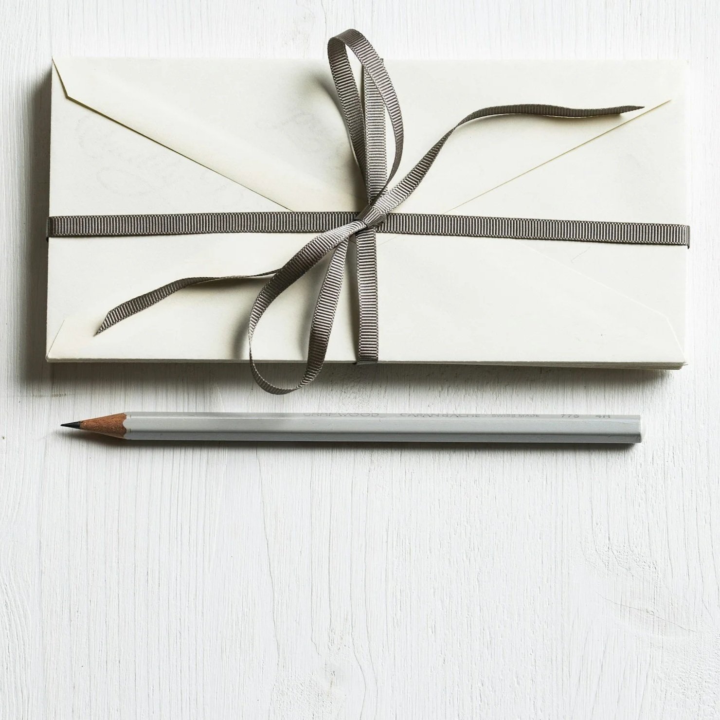 A vase with white daisies and orange marigolds, a bowl of green peas, and a glass container with yellow flowers on a wooden table, with a stone wall and framed picture in the background.
