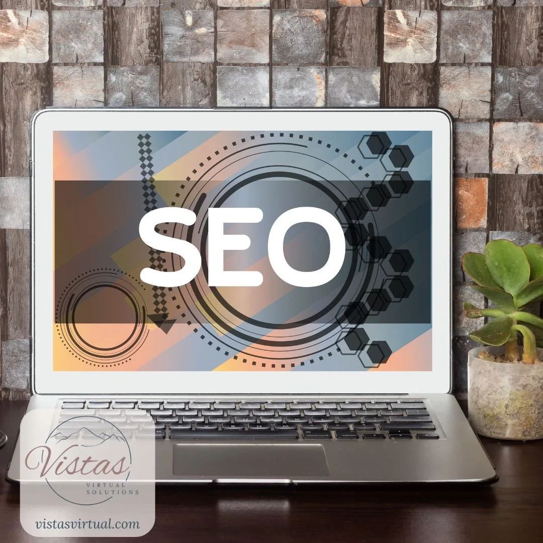 Laptop displaying a graphic with the word 'SEO' on the screen, situated on a desk with plant and stone wall background.