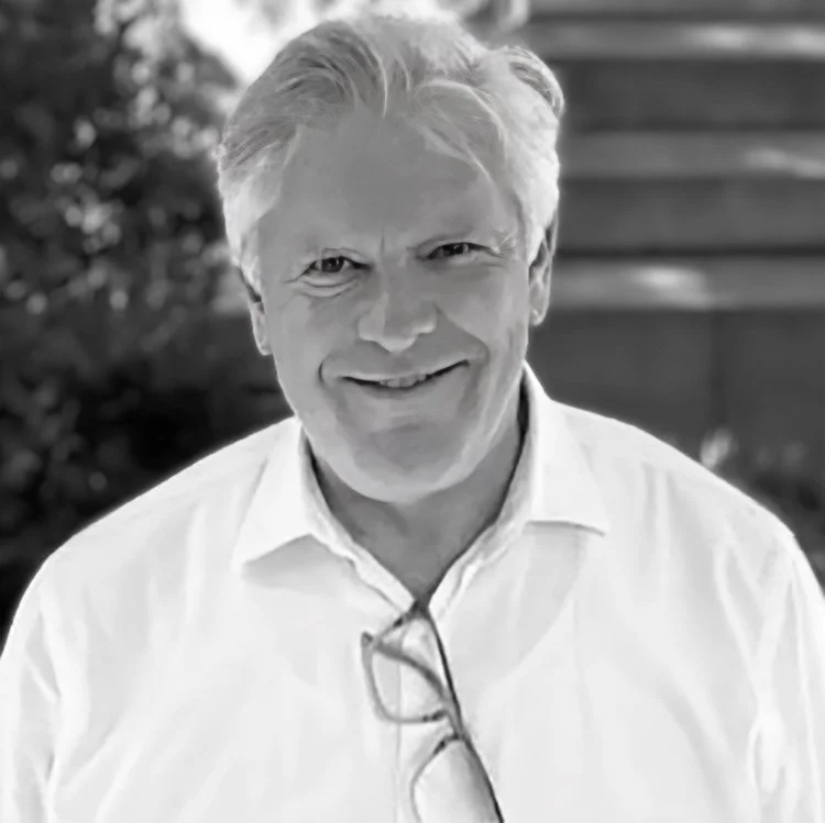 Black and white photo of a smiling middle-aged man with light hair, wearing a collared shirt and glasses hanging from the shirt collar.