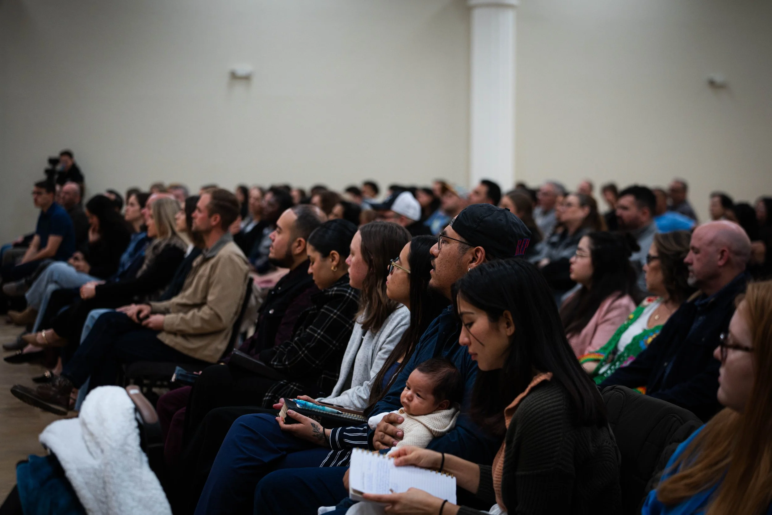 Audience seated at an indoor event, attentively listening to a speaker or presentation.