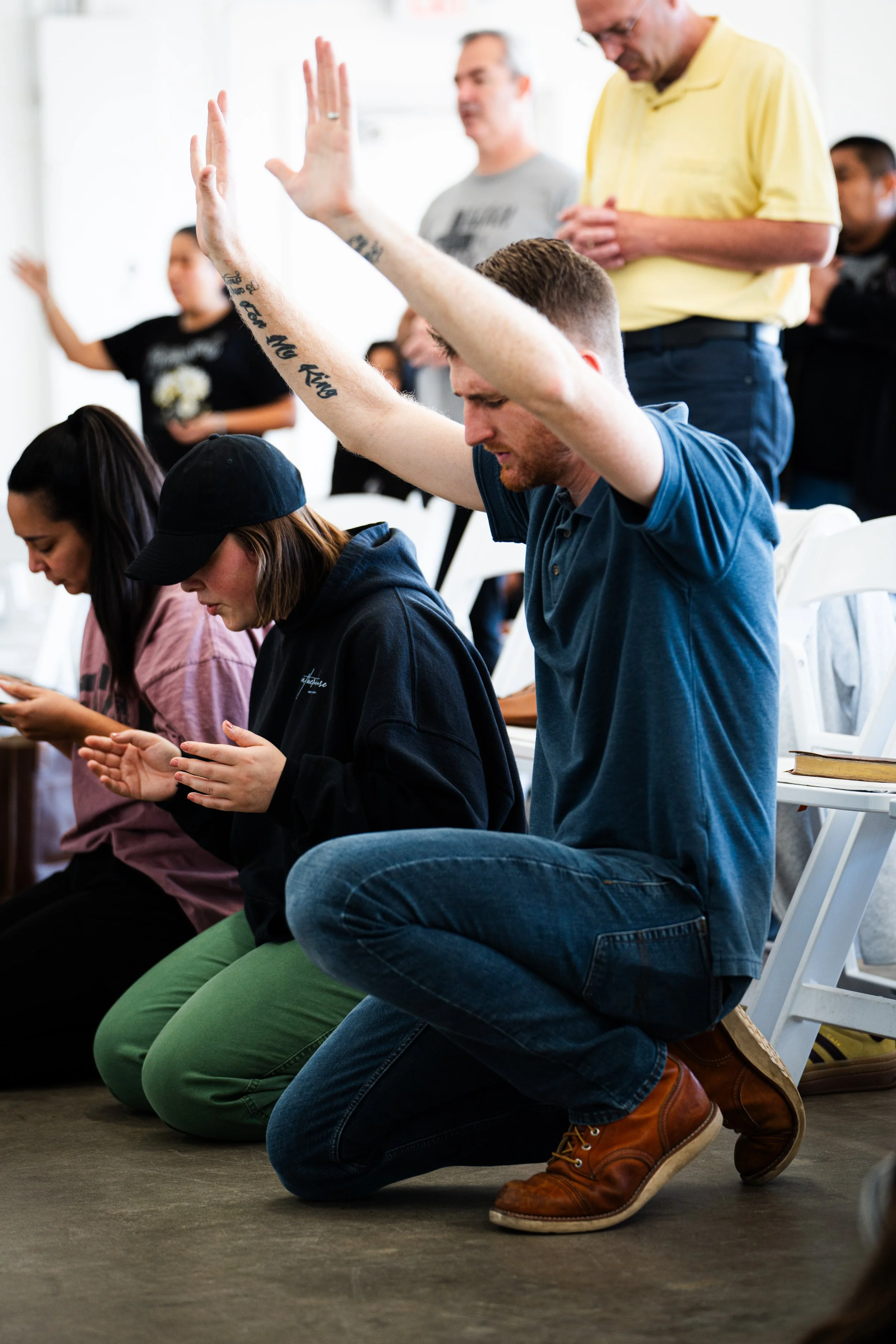 Group of people kneeling and praying with hands raised in a room.
