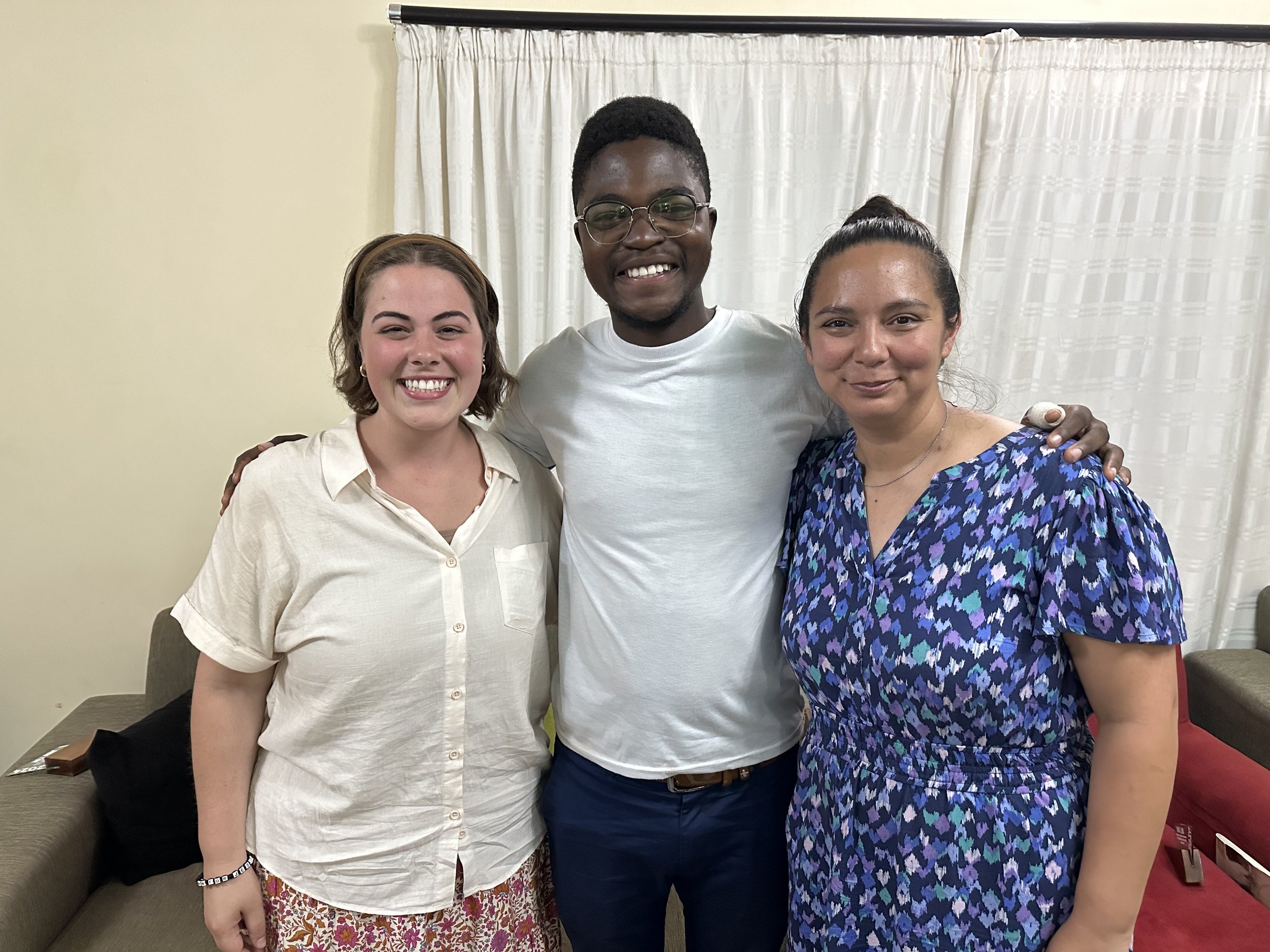 Three people smiling and standing close, posing for a photo indoors with a curtain background.