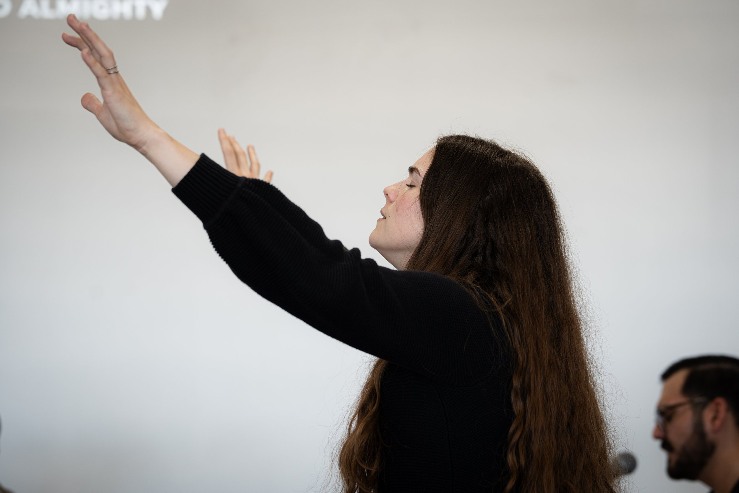 Woman with long brown hair raising her arms in a worship setting.