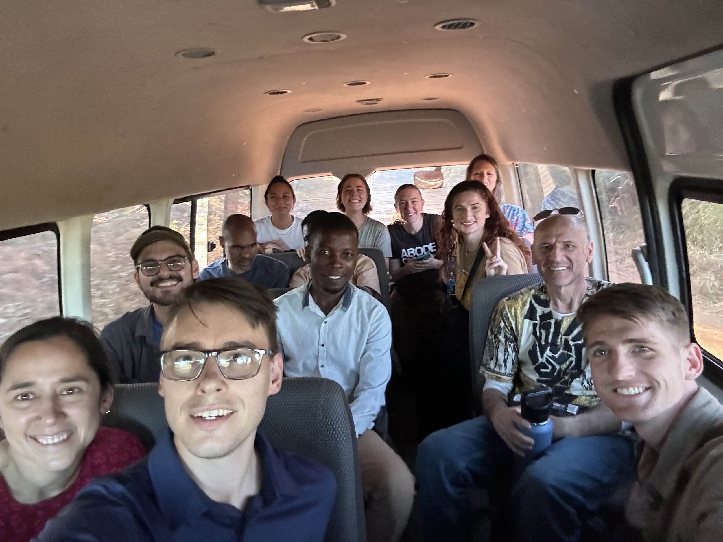 Group of people smiling inside a van, taking a selfie.