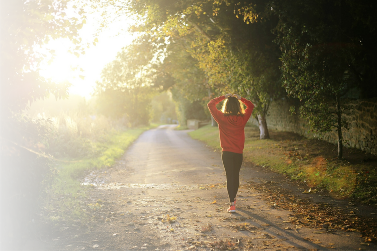 A teen walking away from the camera down a sunlit road