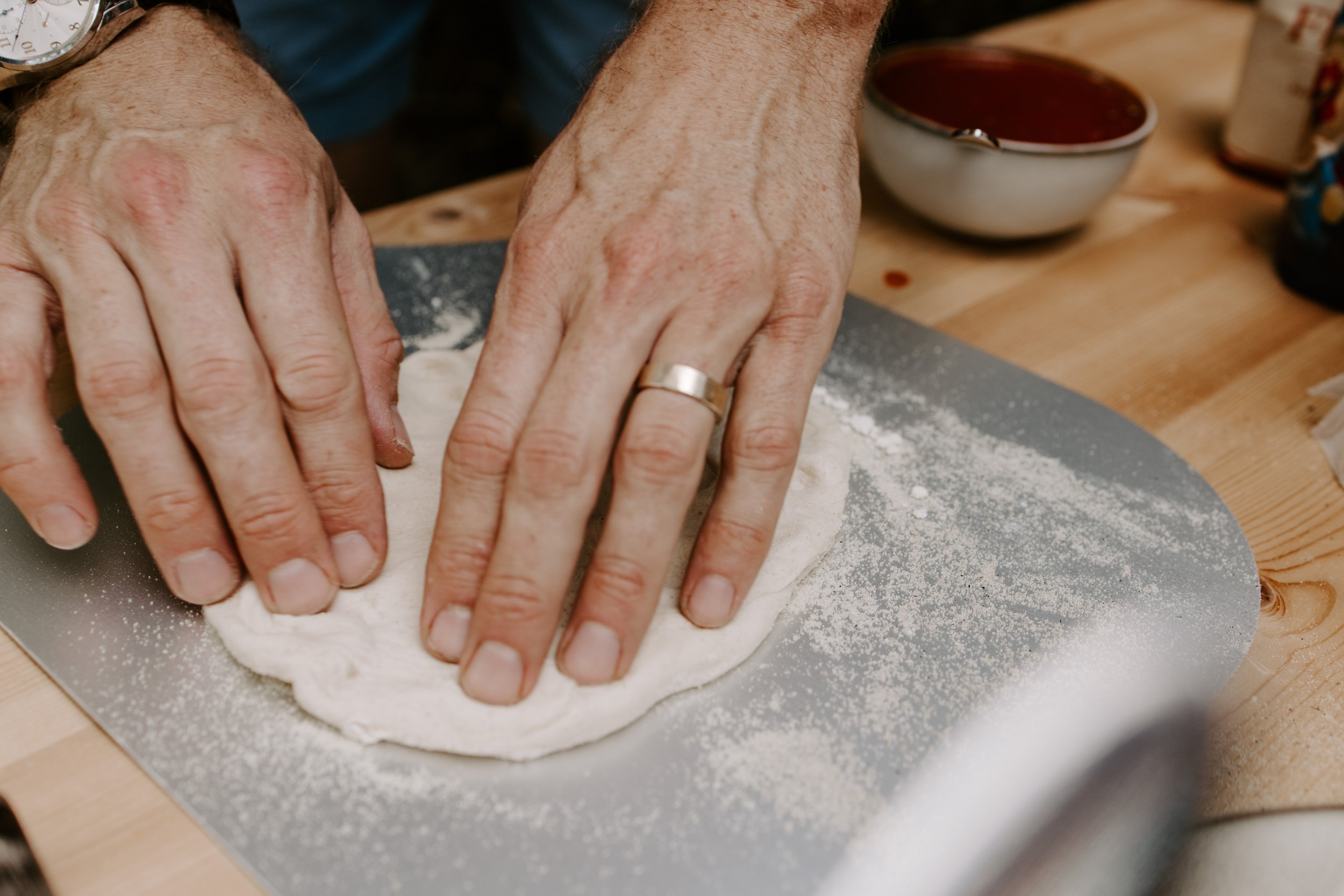 Close-up of hands flattening dough on a countertop Dusting of flour on the dough and surface background with bowls and utensils