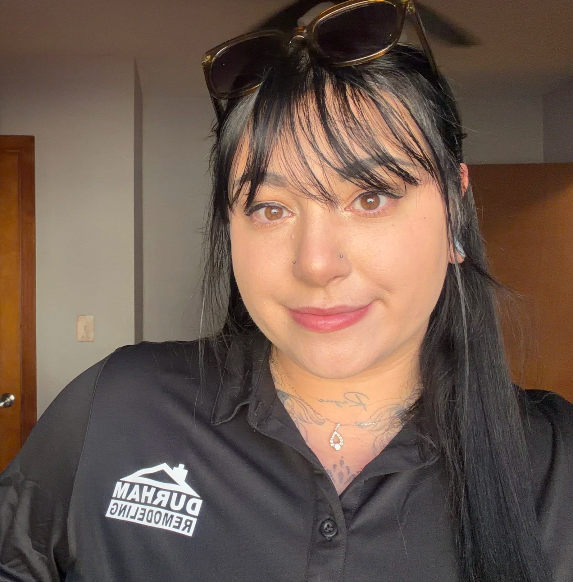 Woman with tattoos and long dark hair smiling indoors.