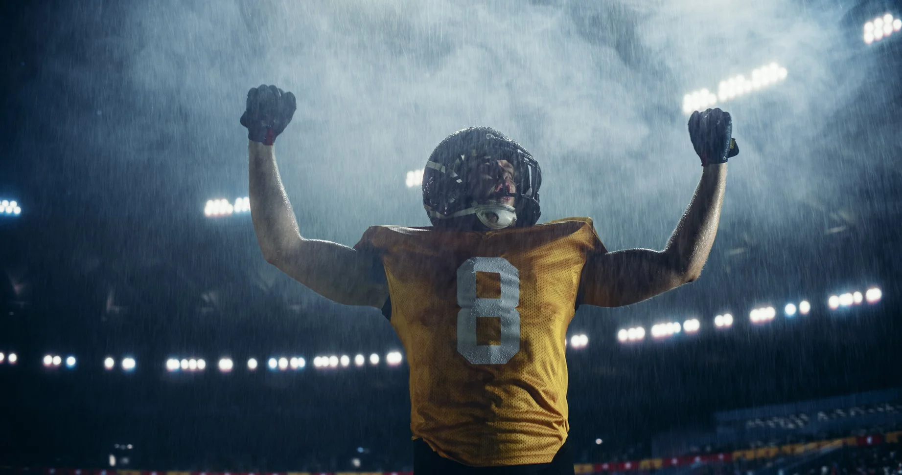 An American football player, in an area, arms raised in victory.