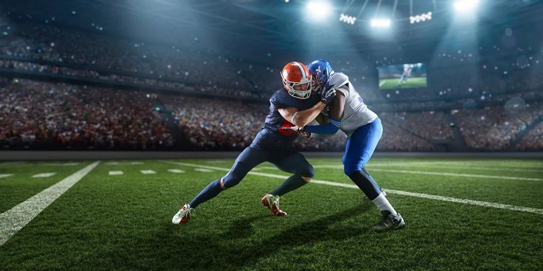 Two American footballs players, on the field, blocking.