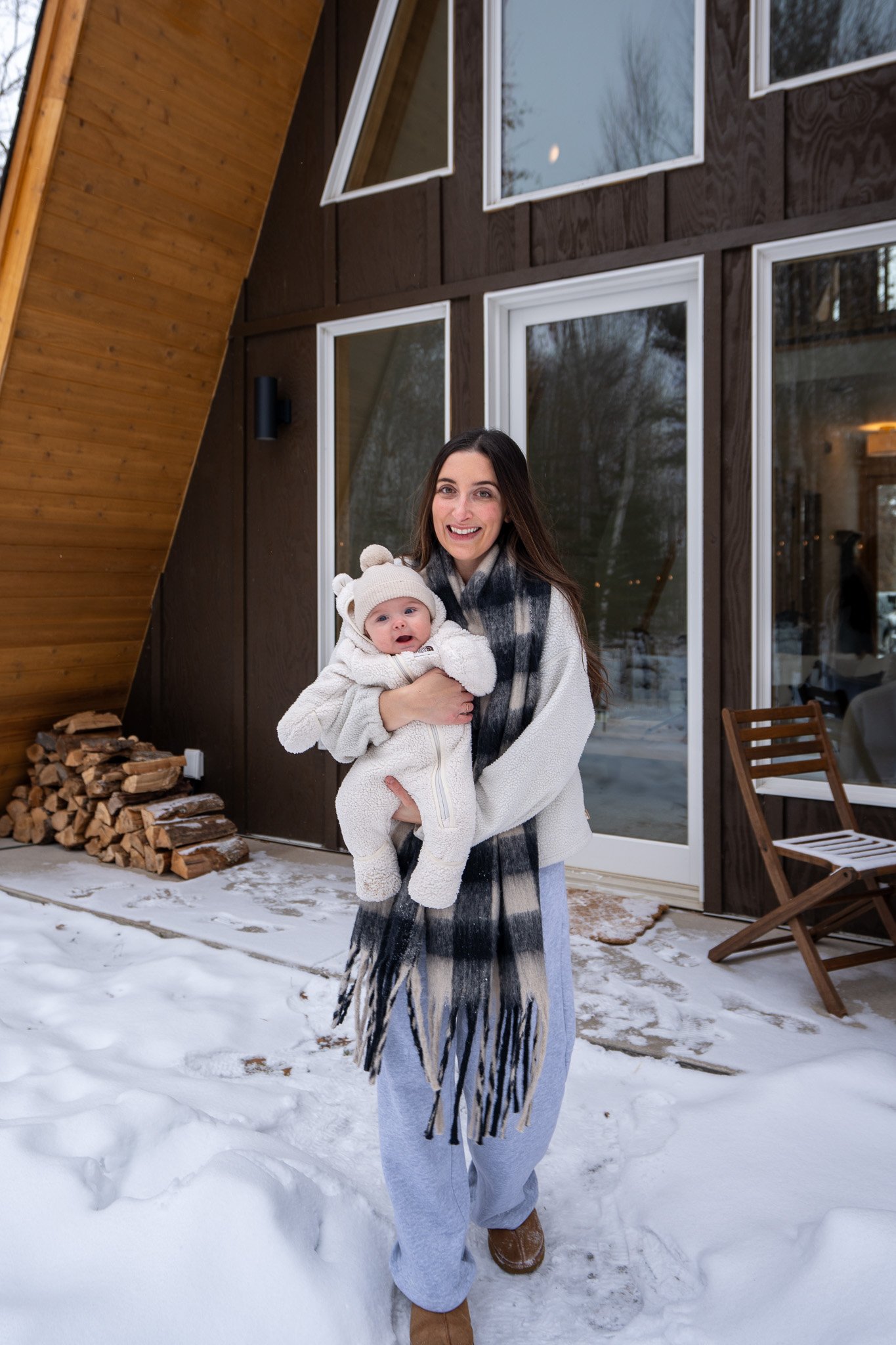 A woman holding a smiling baby outside a snow-covered house.