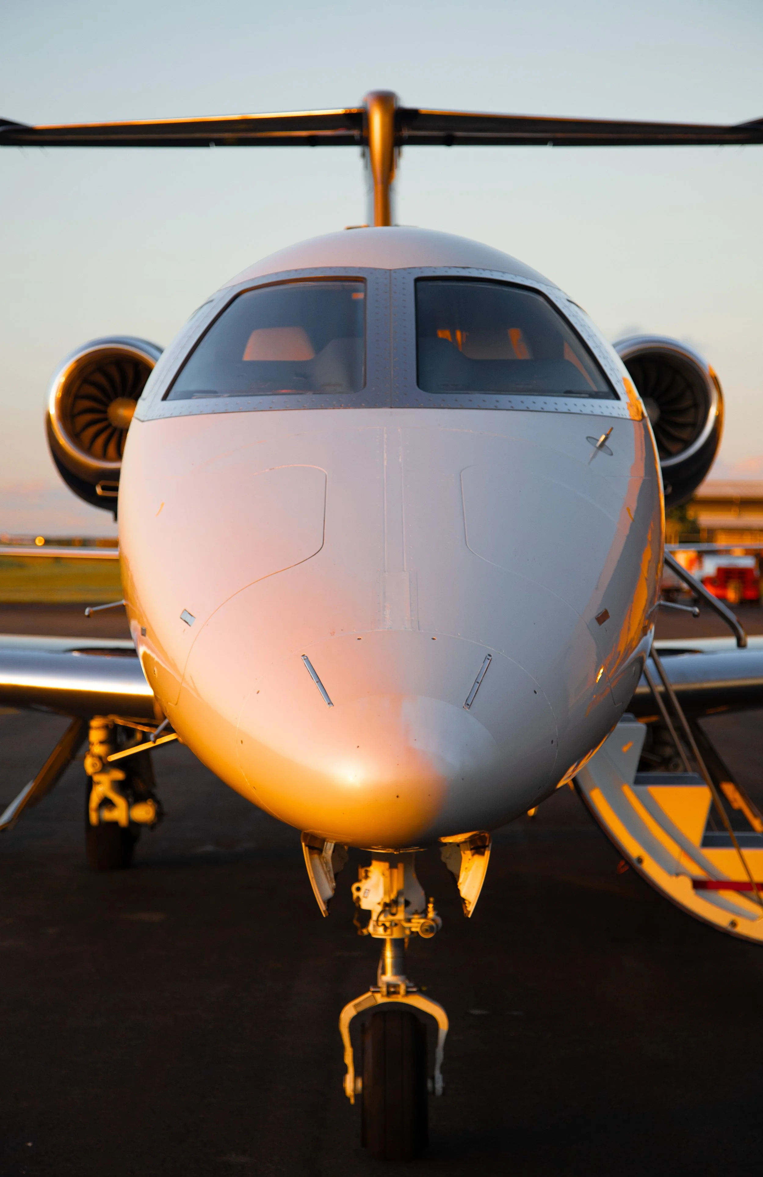 Front view of a private jet on a runway at sunrise or sunset.