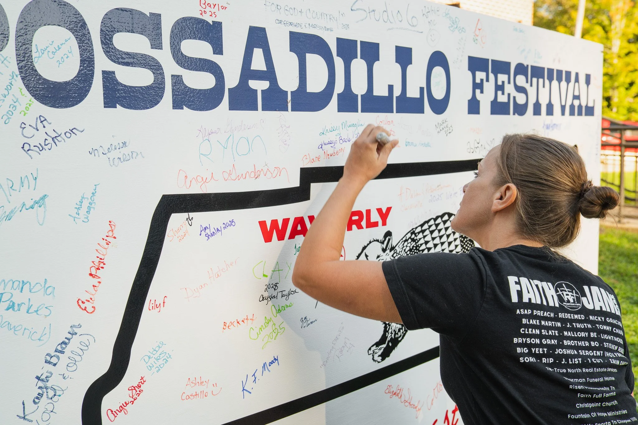A woman signs a large white wall at the possadillo Festival and 5k