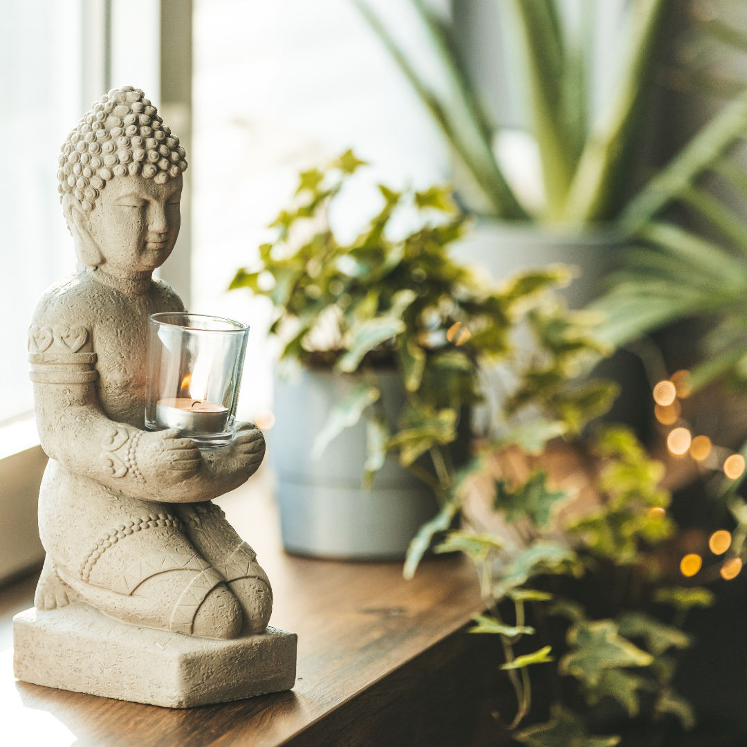 Buddha statue holding a lit candle surrounded by plants, symbolizing inner peace and mindfulness