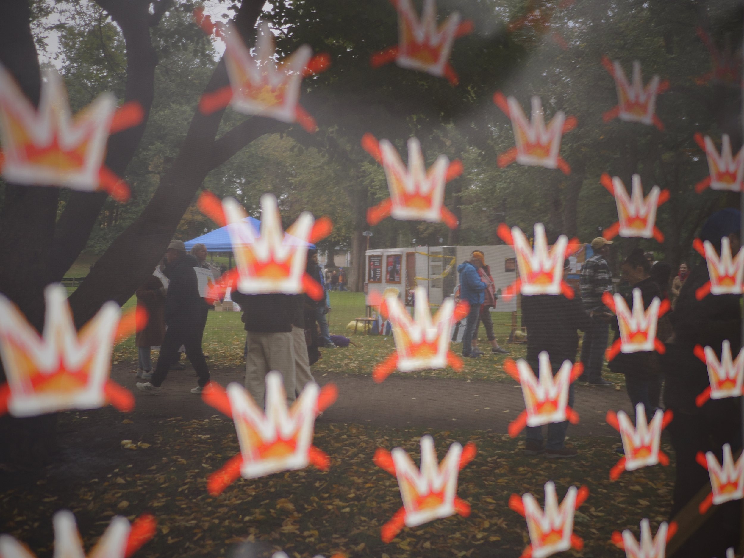 An art installation consisting of a series of walls with political imagery, viewed through a translucent banner with crossed out crowns on it to signify No Kings.