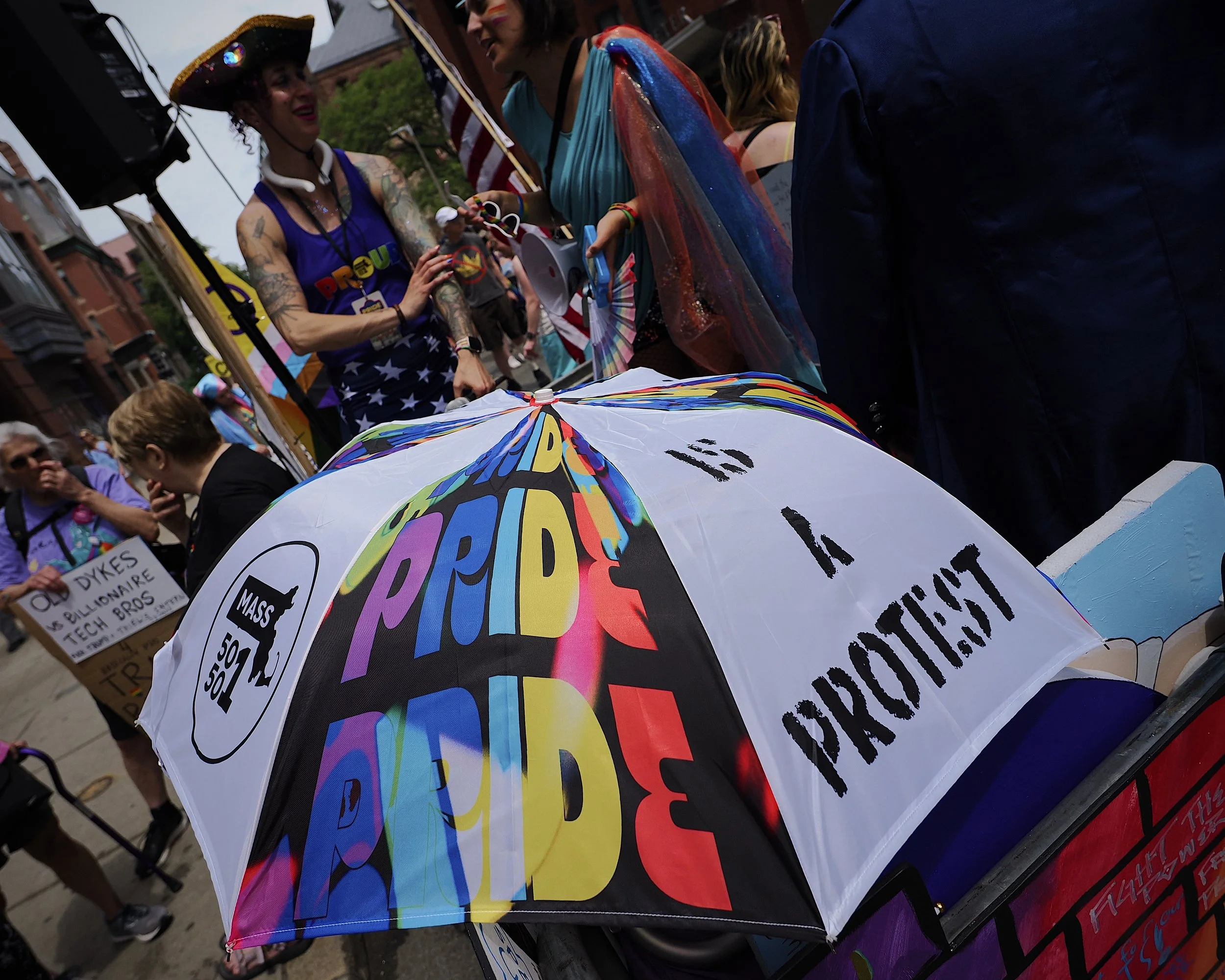 An umbrella that says “Pride is a protest” on a parade float with people in the background.