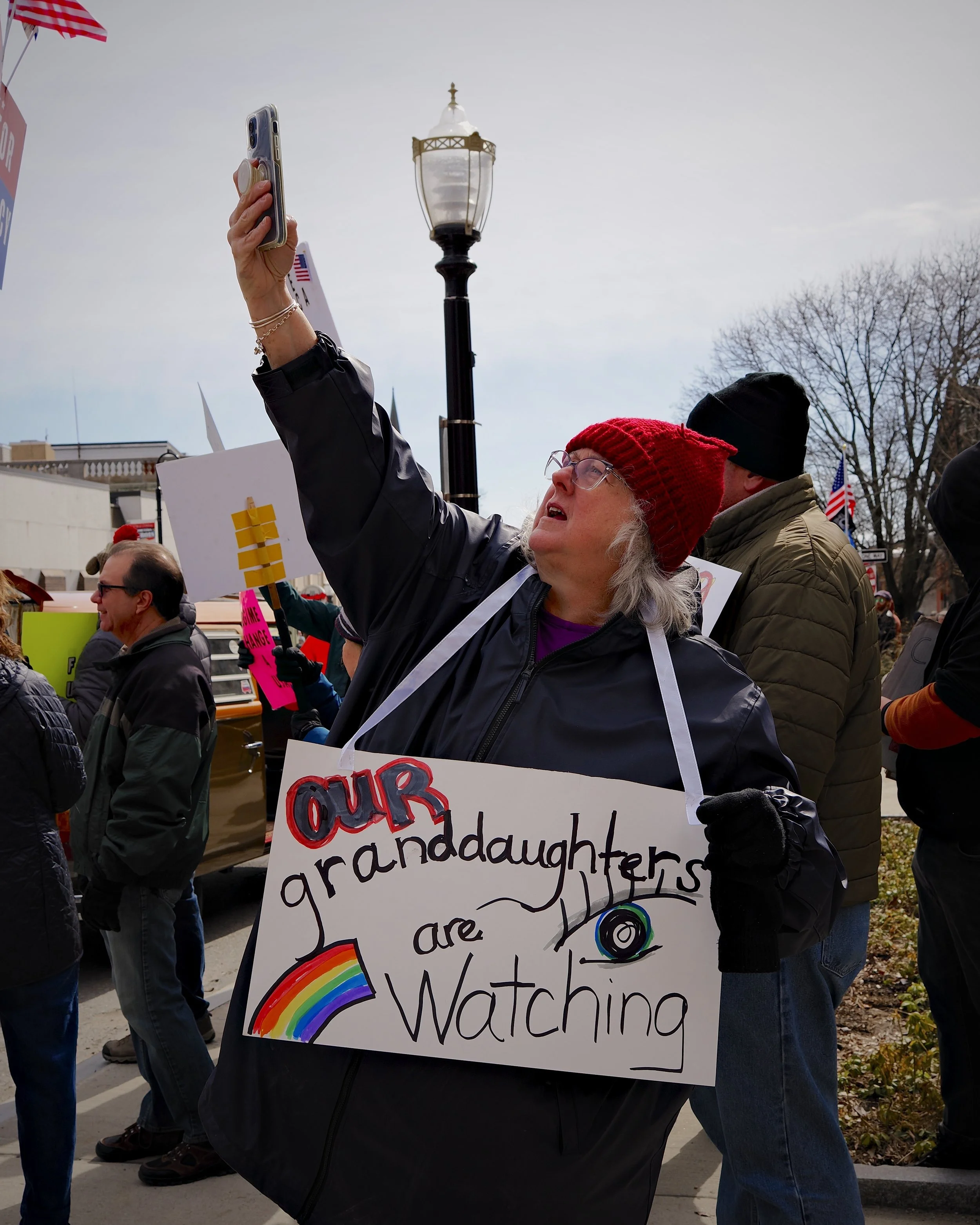 Older woman holding sign that says "Our granddaughters are watching" at No Kings III in Fitchburg by Mass 50501.