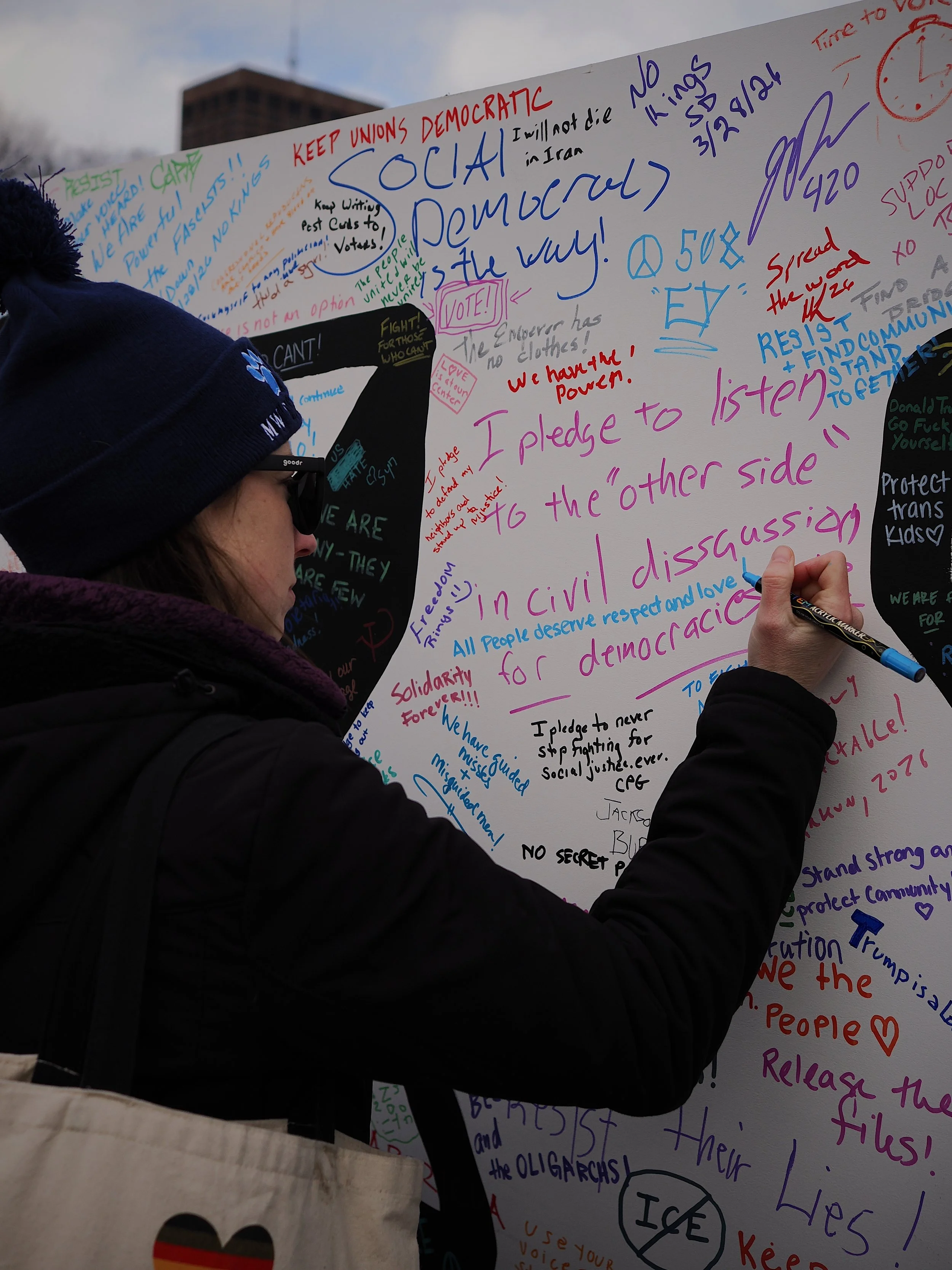 A person writing “all people deserve respect and love” on a board filled with additional messages, including “I pledge to listen to ‘the other side’ in civil discussion”.