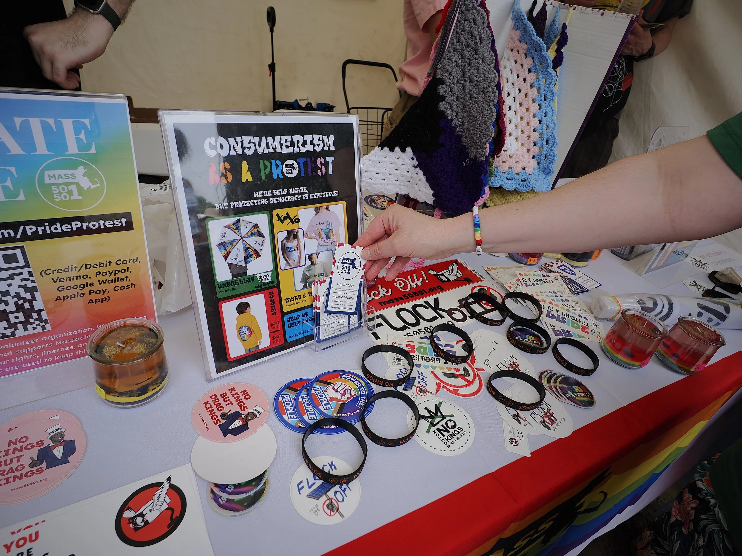 Bracelets and stickers, including several stickers with the motto “Flock off” on a table with a rainbow-colored flag hanging from the front.