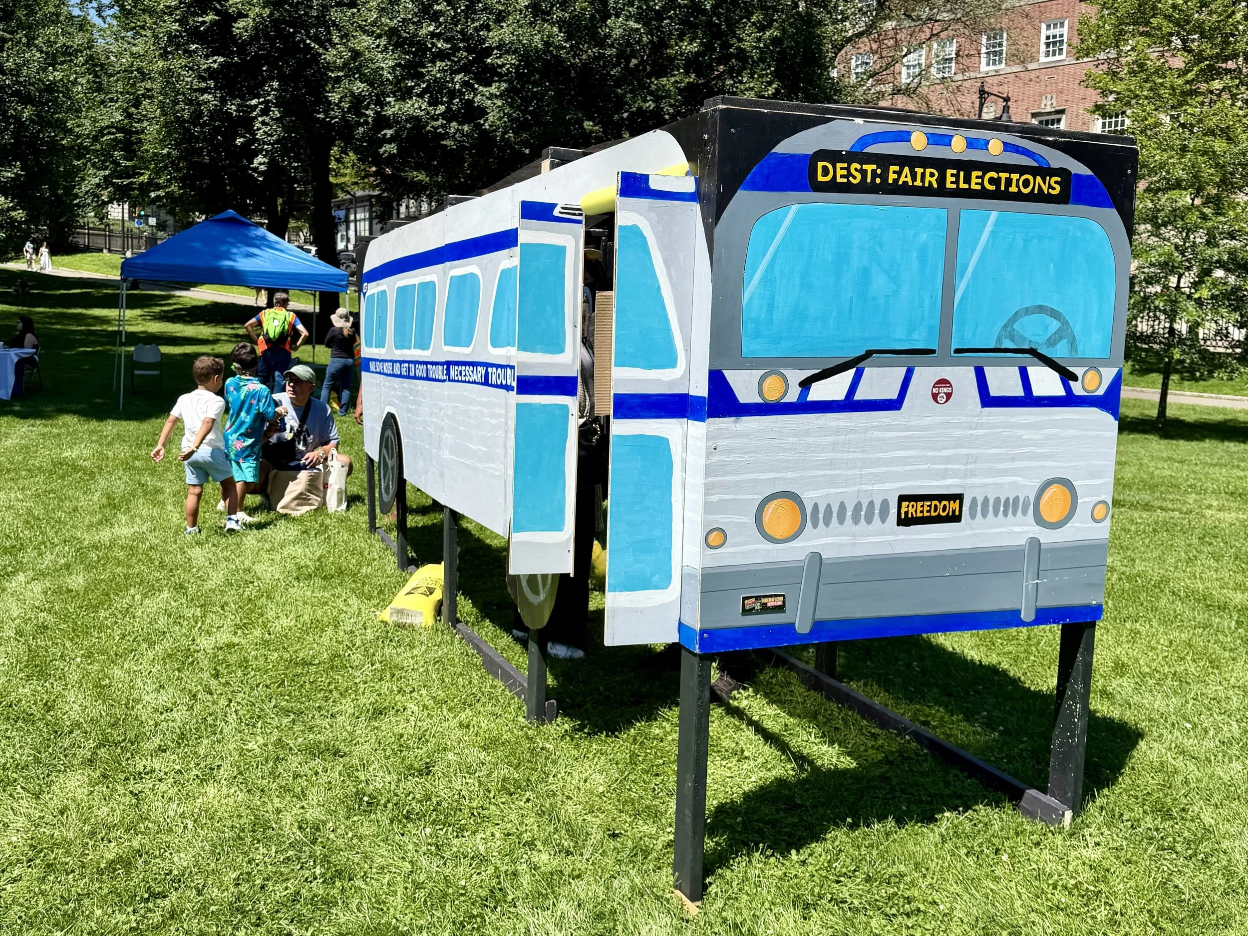A plywood model of a bus with “Dest: Fair Elections” written on the front above the windshield, “FREEDOM” as the license plate, and “Make some noise and get in good trouble, necessary trouble” written along the side.