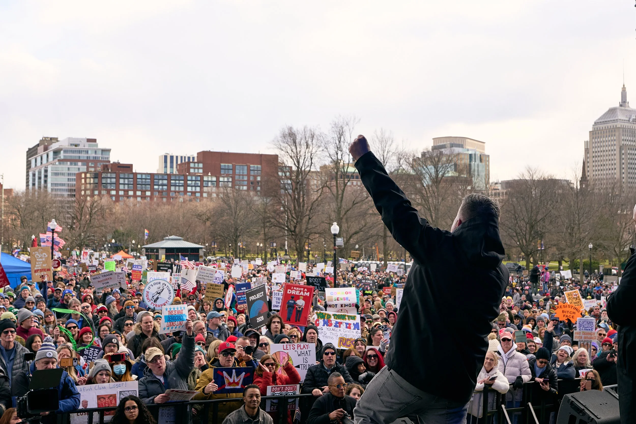 Lead singer of Dropkick Murphys raising his fist in the air at a large crowd of people with protest signs at No Kings III in Boston by Mass 50501.