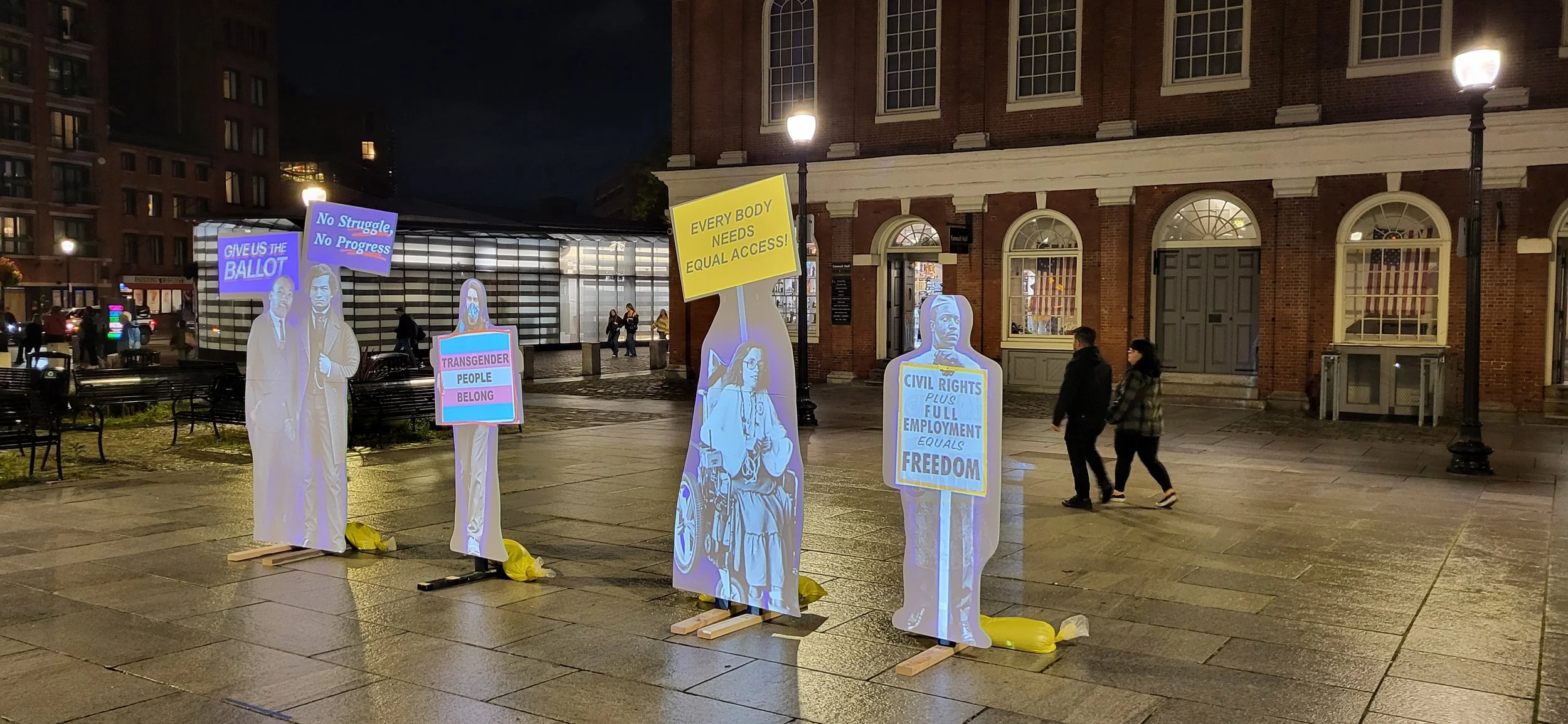 Projections with signs: MLK Jr. with “Give Us the Ballot”, Frederick Douglass with “No Struggle, No Progress”, and protestors with “Transgender People Belong”, “Every Body Needs Equal Access”, and “Civil Rights Plus Full Employment Equals Freedom”.