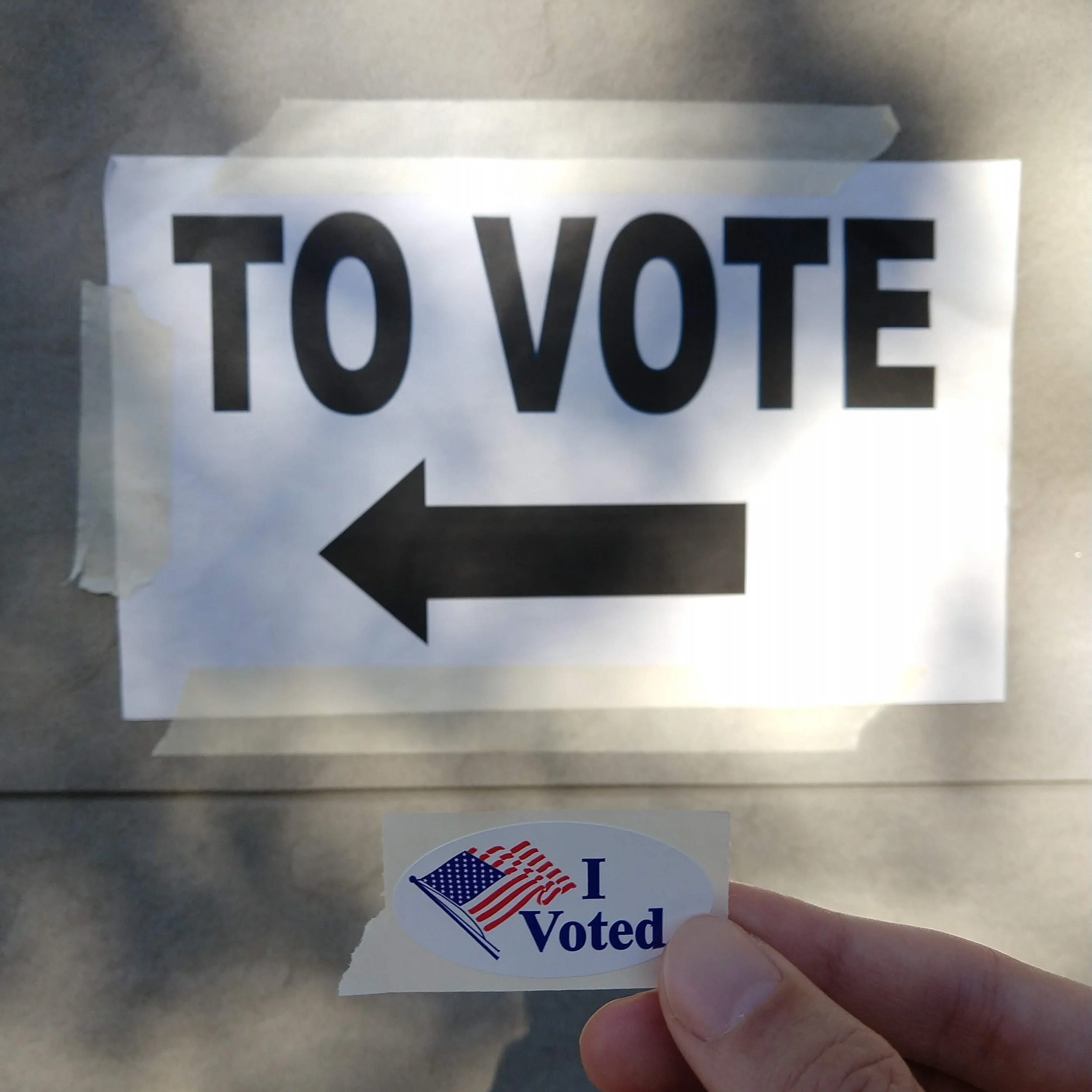A sign that read "TO VOTE" with someone holding an "I voted" sticker in front of it.