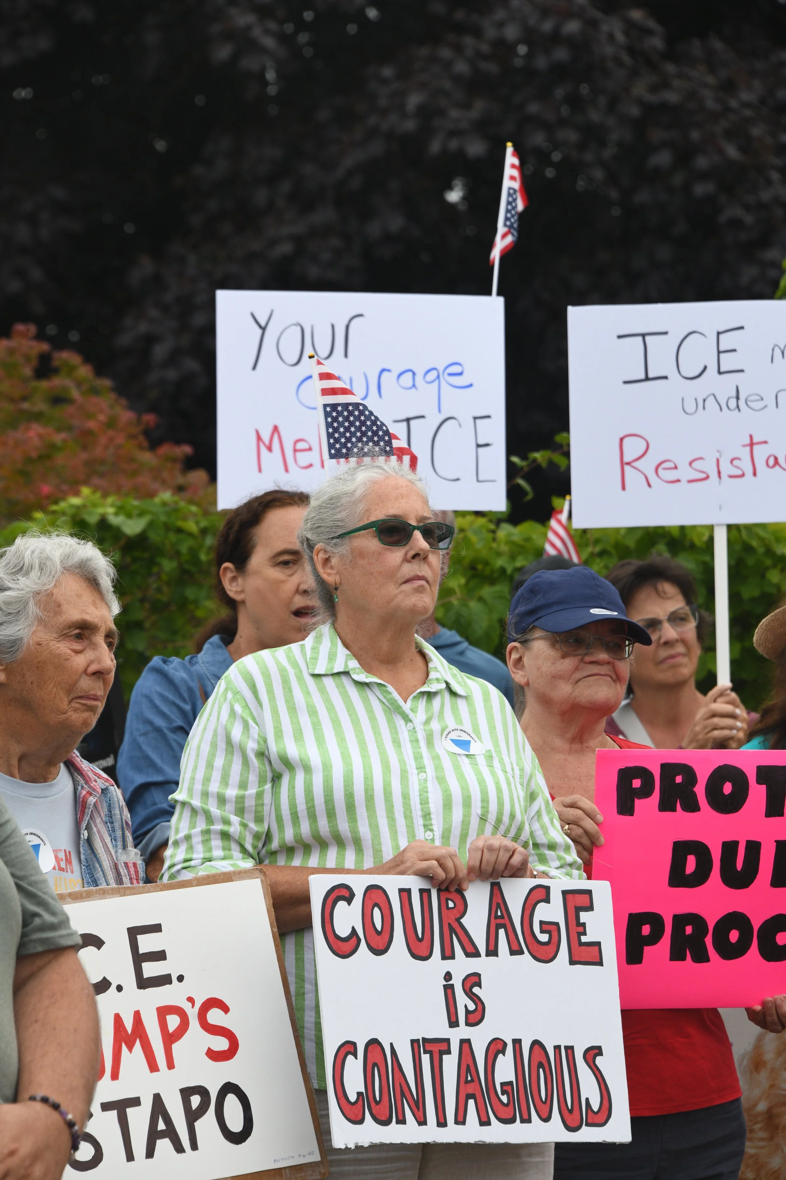 A group of people holding signs, one of which says, “Courage is contagious.”