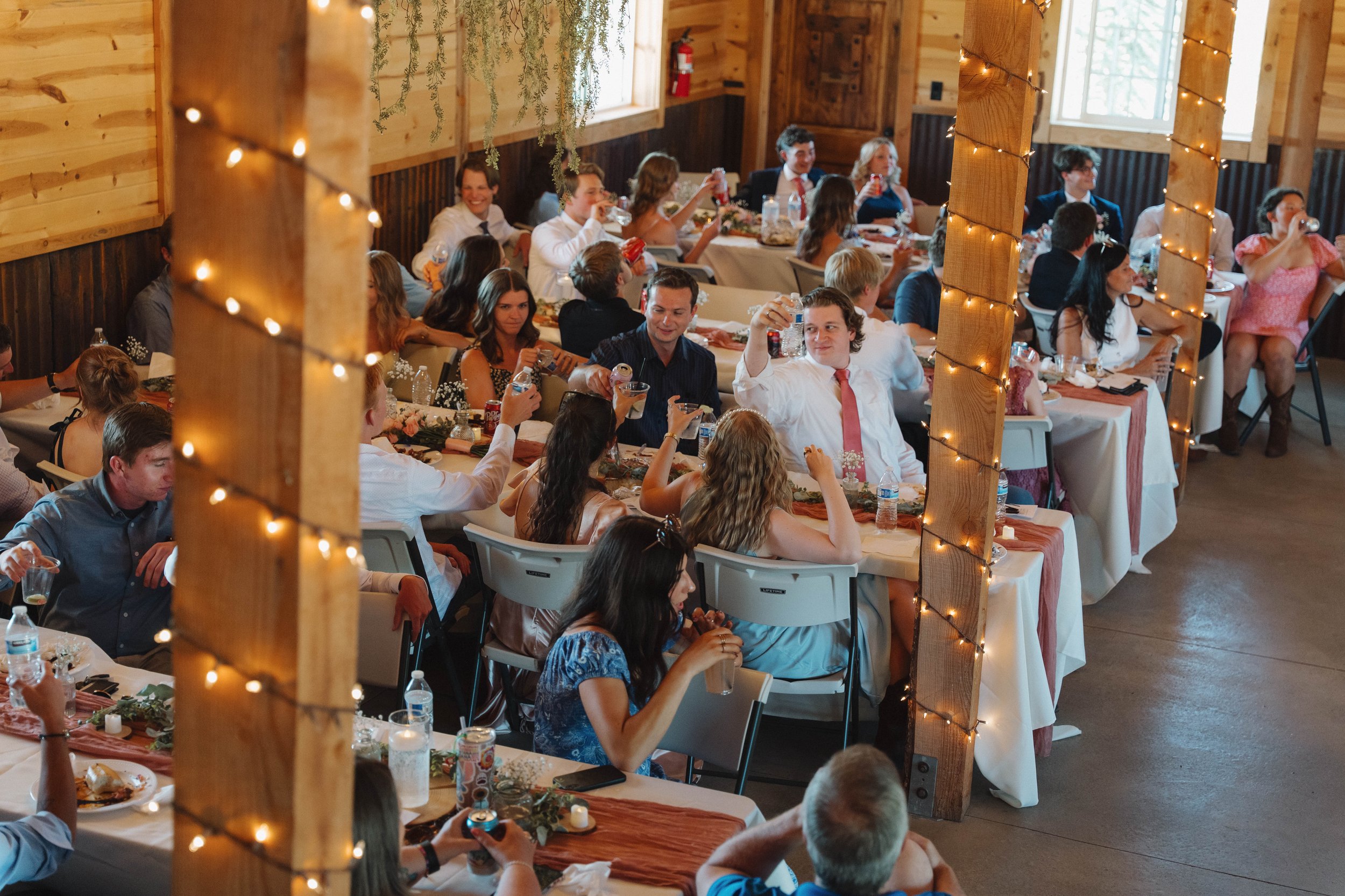 People sitting at decorated tables in a rustic indoor setting, celebrating with drinks and food.