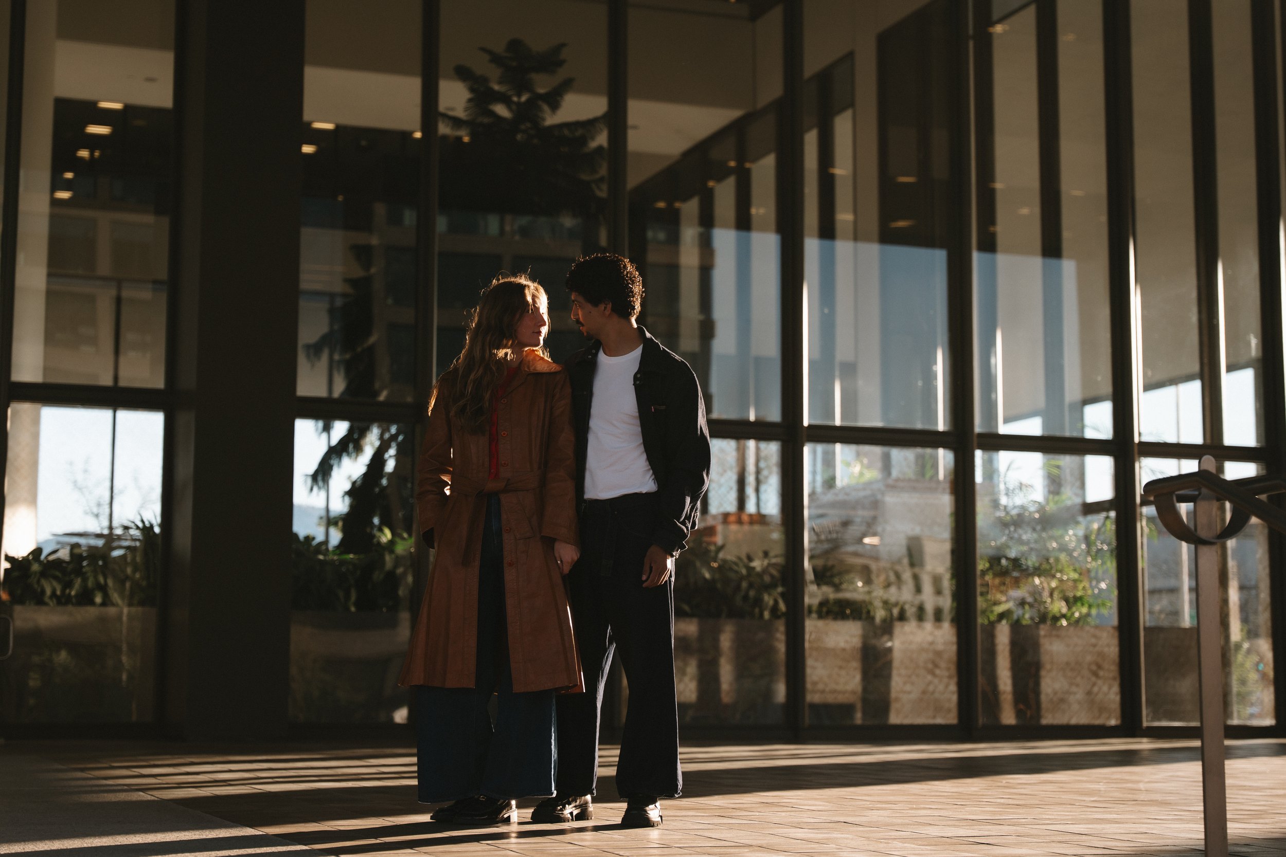 A man and woman standing close together inside a modern building with large glass windows during daytime.